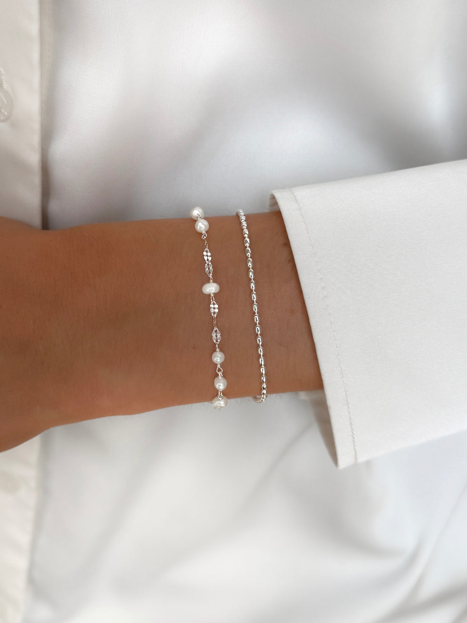 A close-up of a model wearing the Aurelia & Lunetta Bracelet Set in silver, featuring the delicate pearl-adorned Aurelia bracelet stacked with the simple Lunetta chain bracelet.