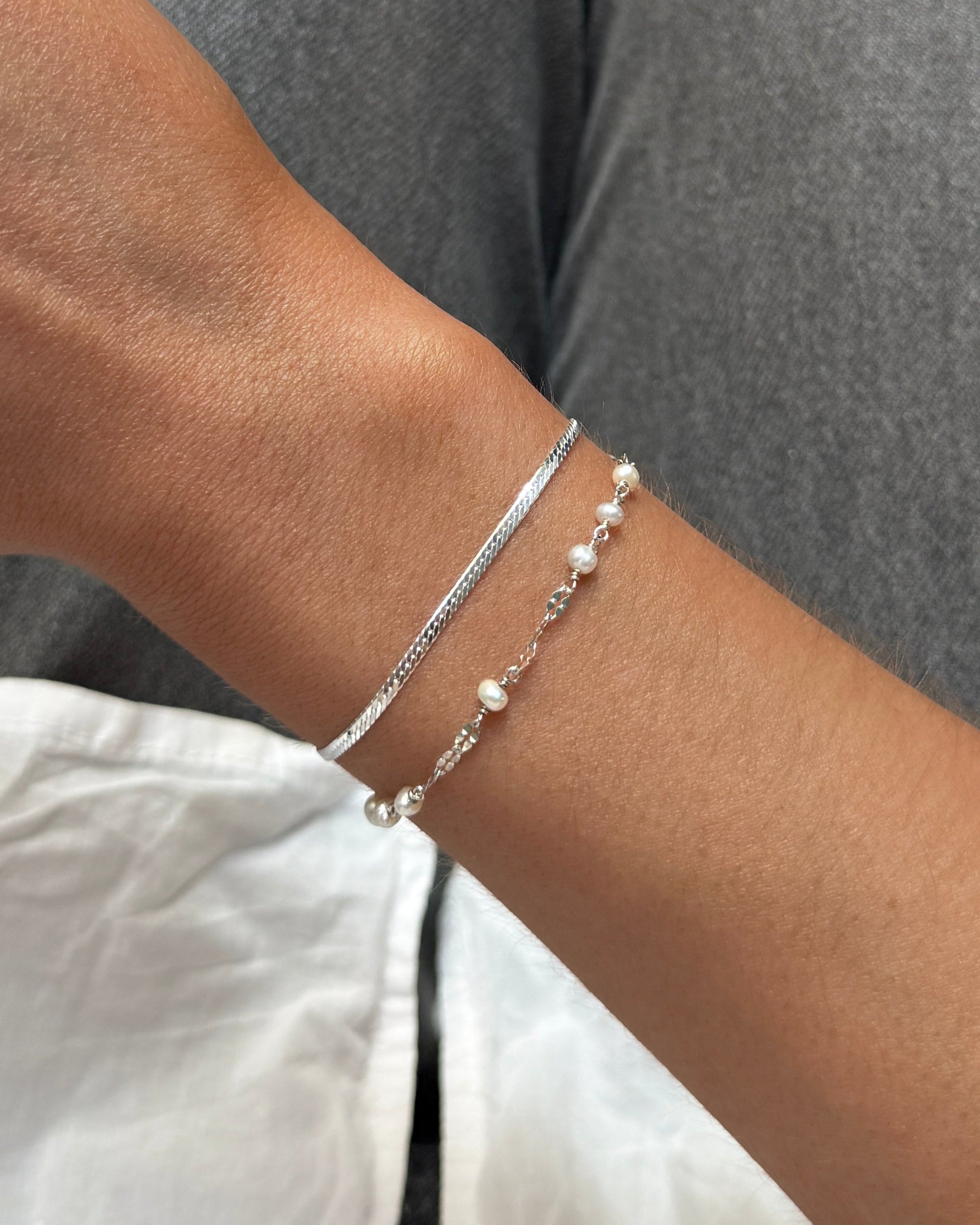 Two silver bracelets, one with small beads and silver details and the other a flat silver bracelet.