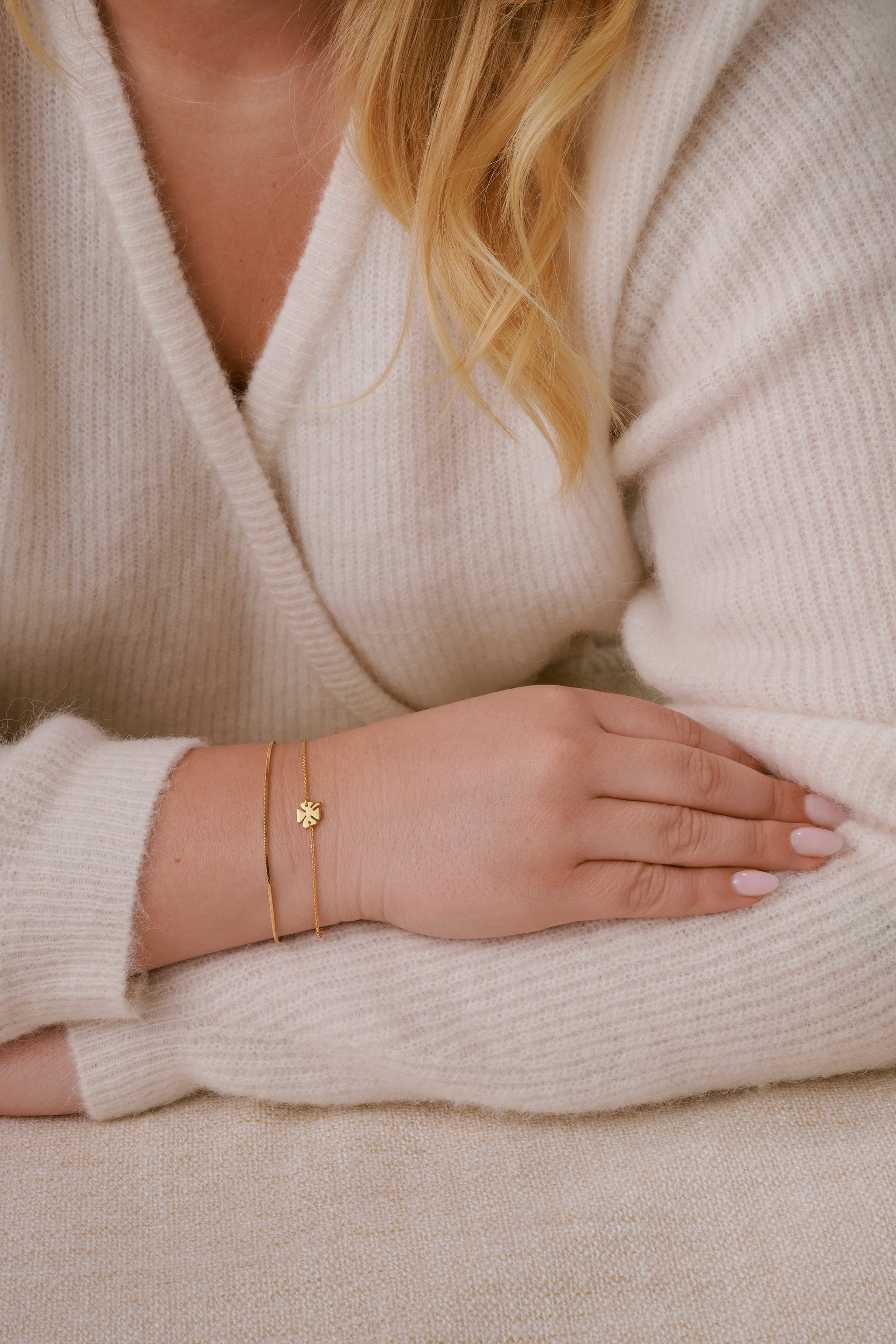 A close-up of a model's wrist wearing the Bring Me Luck Bracelet in gold, featuring a delicate chain and a four-leaf clover charm, styled with Sheer Mirror Bracelet in gold, showcasing its delicate and smooth snake chain.