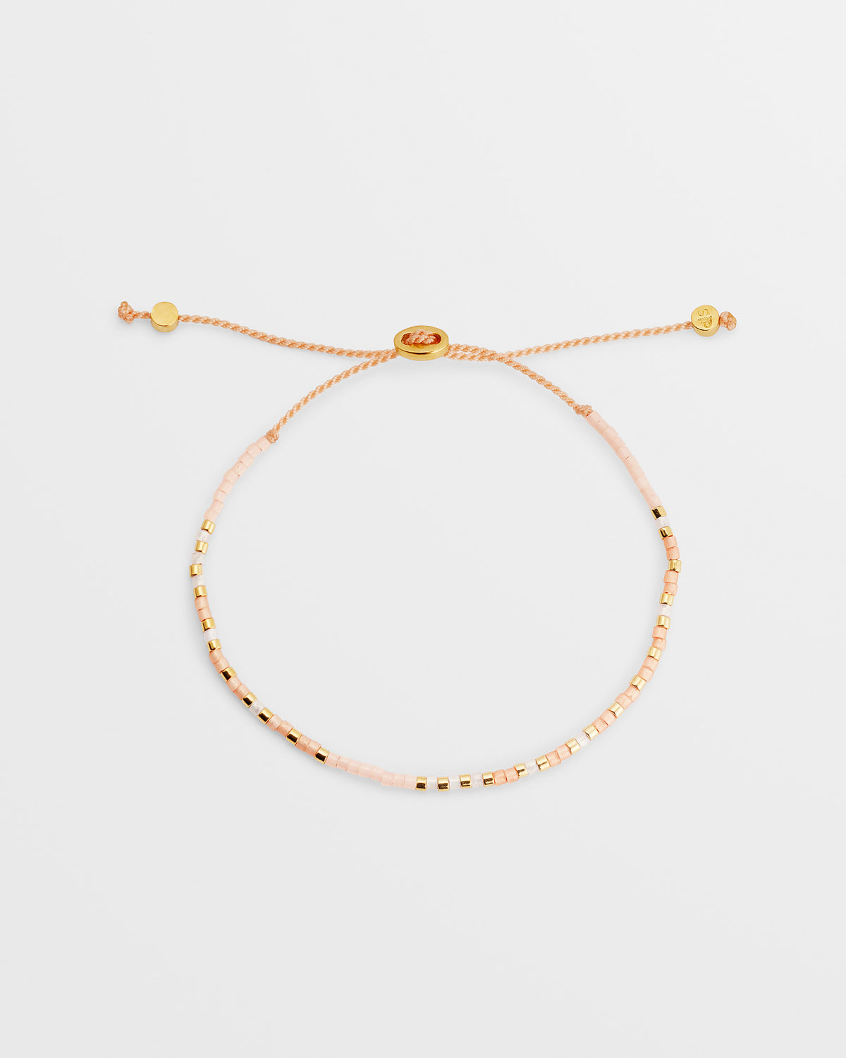 A product shot of the Code Bracelet Gold Stay Strong, showing its design of pink and gold morse code beads on a delicate peach cord with an adjustable gold clasp.