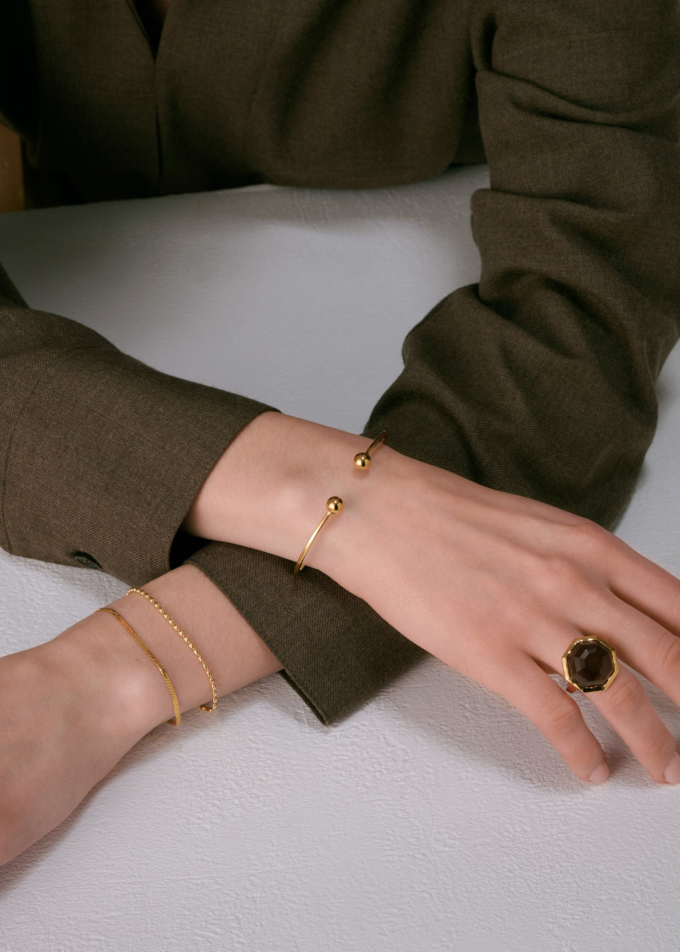 Gold open bangle with ball ends, two delicate gold chain bracelets, and a large gold ring with a dark smoky quartz octagonal stone.
