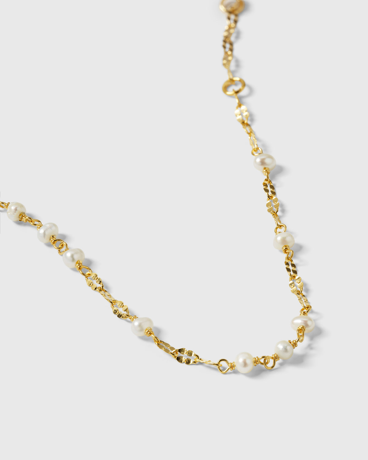 A close-up product shot of the Aurelia Bracelet in gold, highlighting the detail of its unique chain and small freshwater pearls.