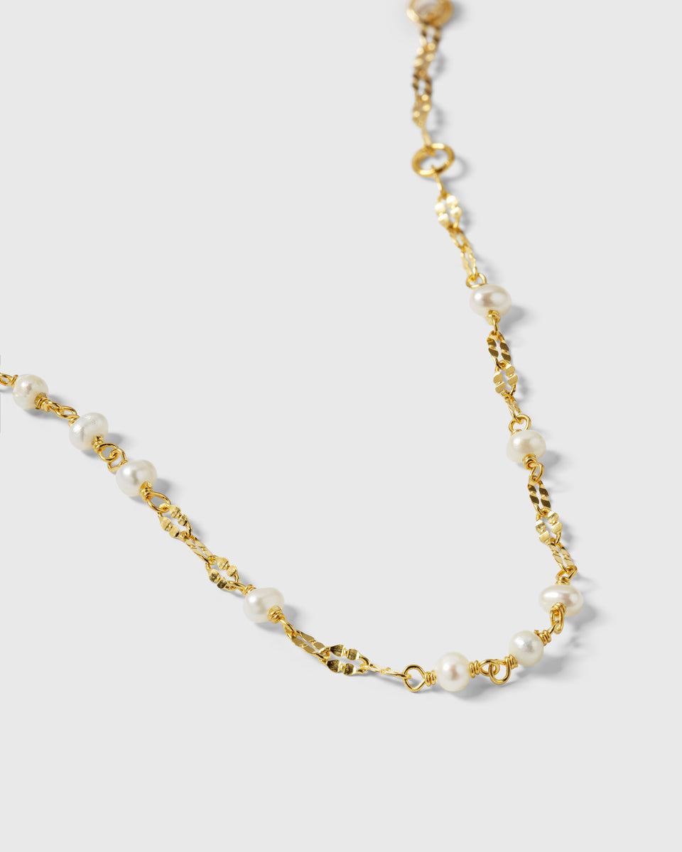 A close-up product shot of the Aurelia Bracelet in gold, highlighting the detail of its unique chain and small freshwater pearls.