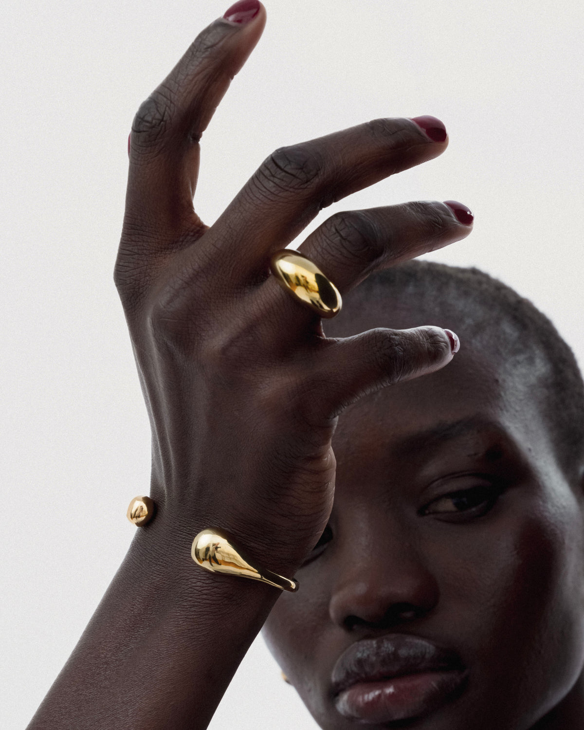 A close-up of a model wearing the Bolded Drops Bangle in gold, showcasing its unique drop-shaped ends, along with a matching chunky gold ring.