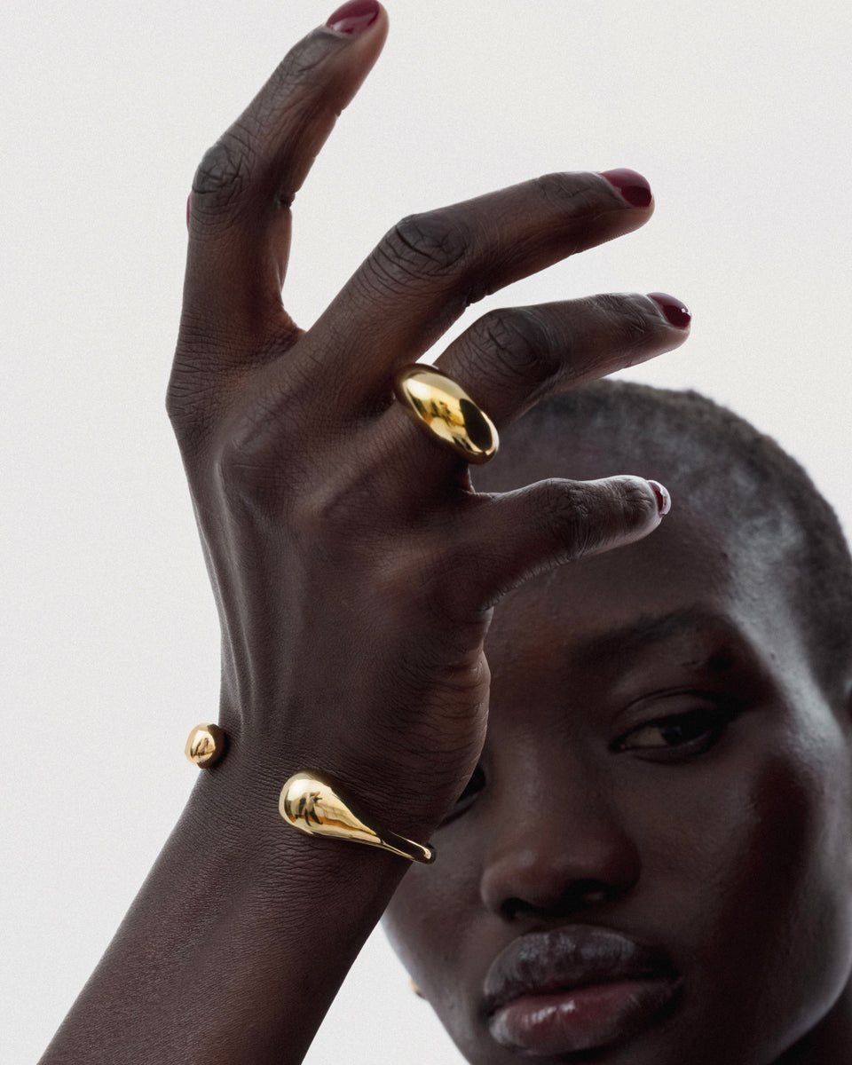 A close-up of a model wearing the Bolded Drops Bangle in gold, showcasing its unique drop-shaped ends, along with a matching chunky gold ring.