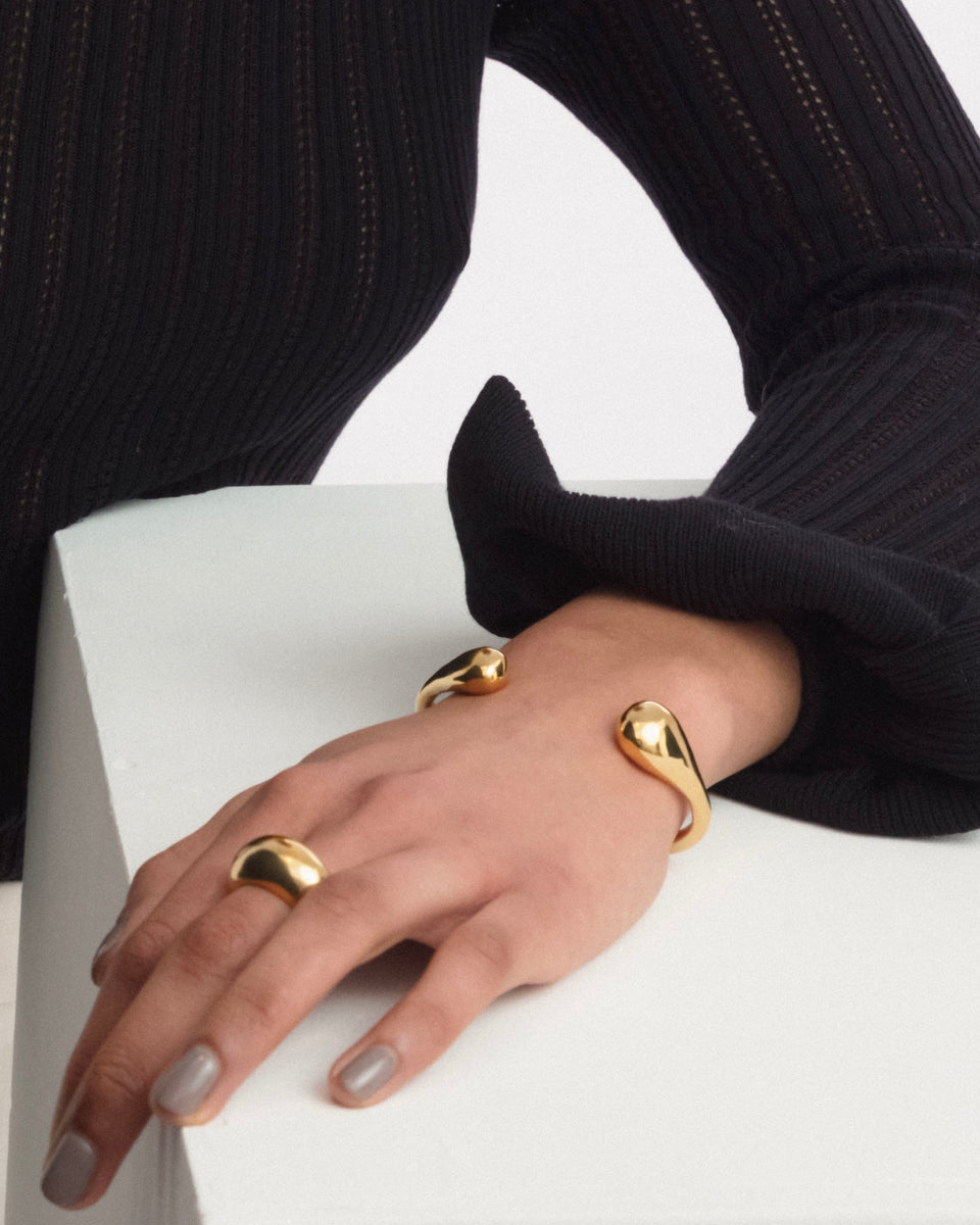 A model wearing the Bolded Drops Bangle in gold, a cuff bracelet with drop-shaped ends, and a matching bold gold ring.