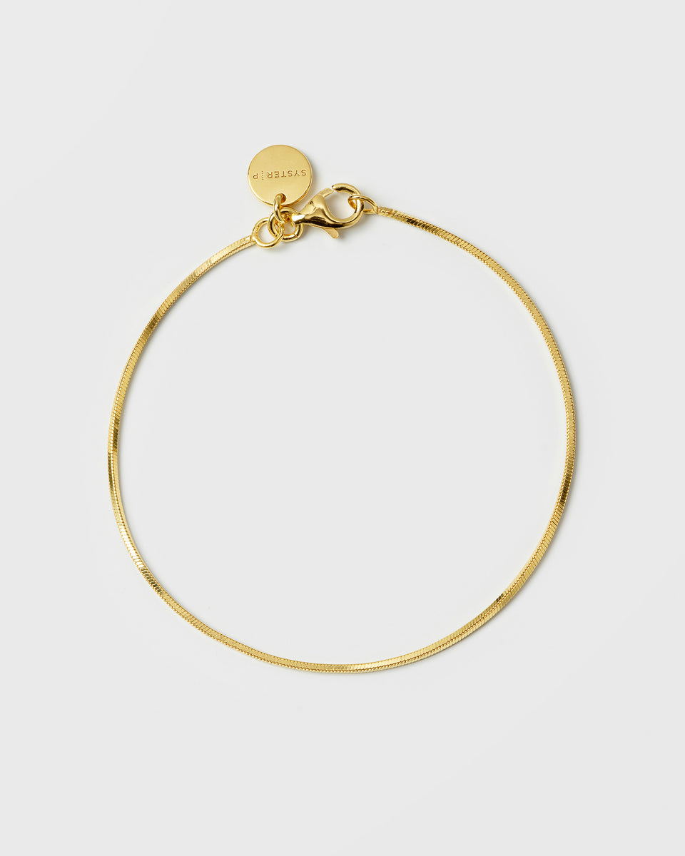 A product shot of the Sheer Mirror Bracelet in gold, laid out in a circle to showcase its delicate and smooth flat chain design, finished with a lobster clasp and a small branded tag.