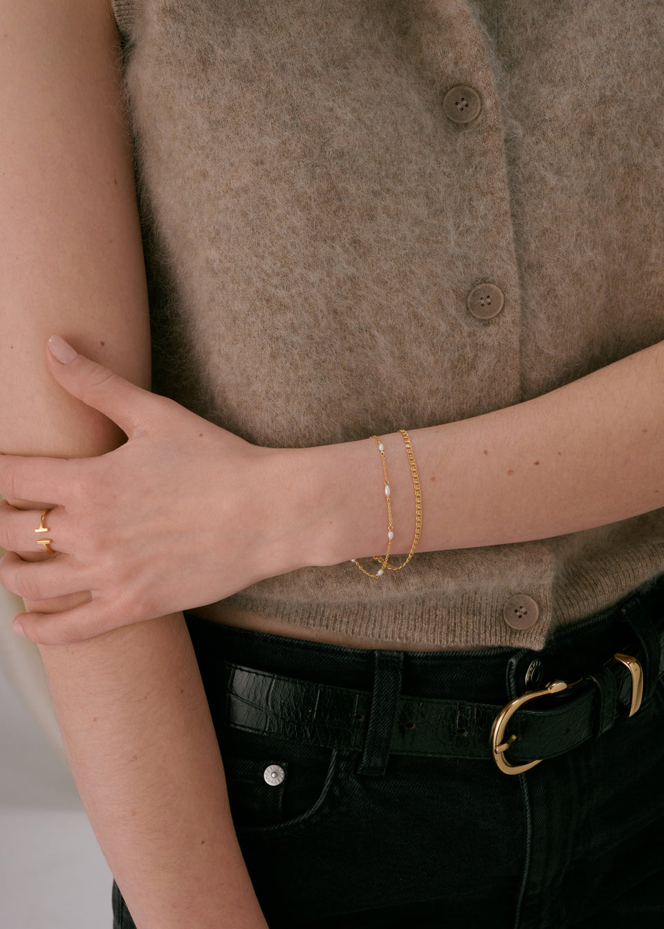A bracelet, stacked with a delicate gold chain bracelet with small pearls.