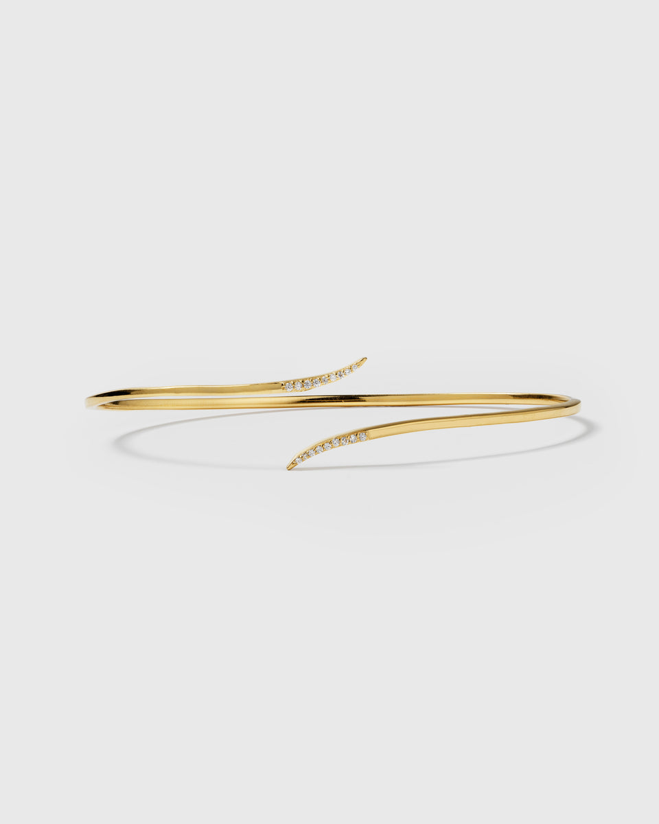 A product shot of the Sparkle Wrap Bangle in gold, showcasing its wrap-around design with curved ends adorned with sparkling cubic zirconia stones.