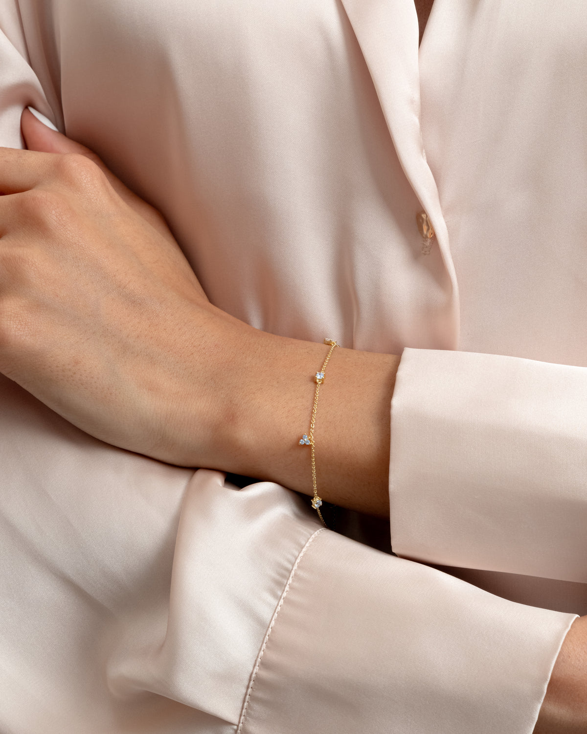 A close-up shot of a model wearing the Celestia Bracelet in gold. The delicate gold chain bracelet is adorned with several small, sparkling cubic zirconias.