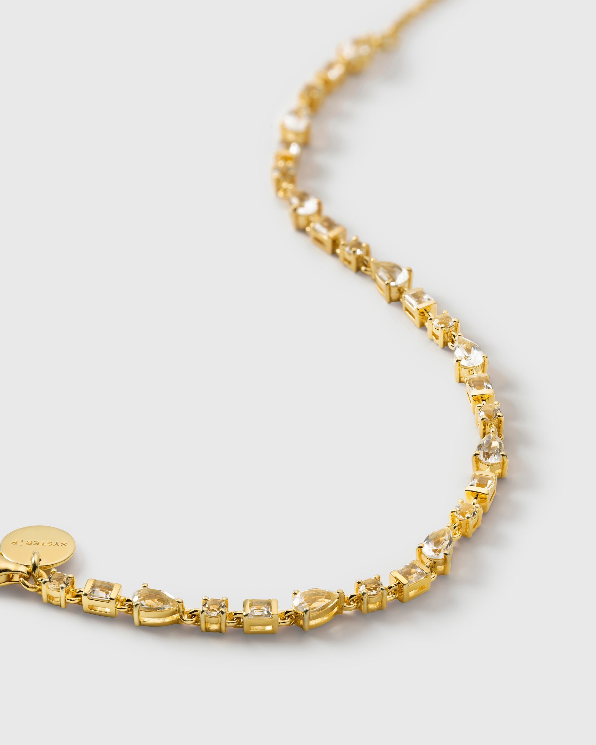 A close-up product shot of the Pam Bracelet in gold, laid out in a curve to showcase its design of small, variously shaped white topaz stones.