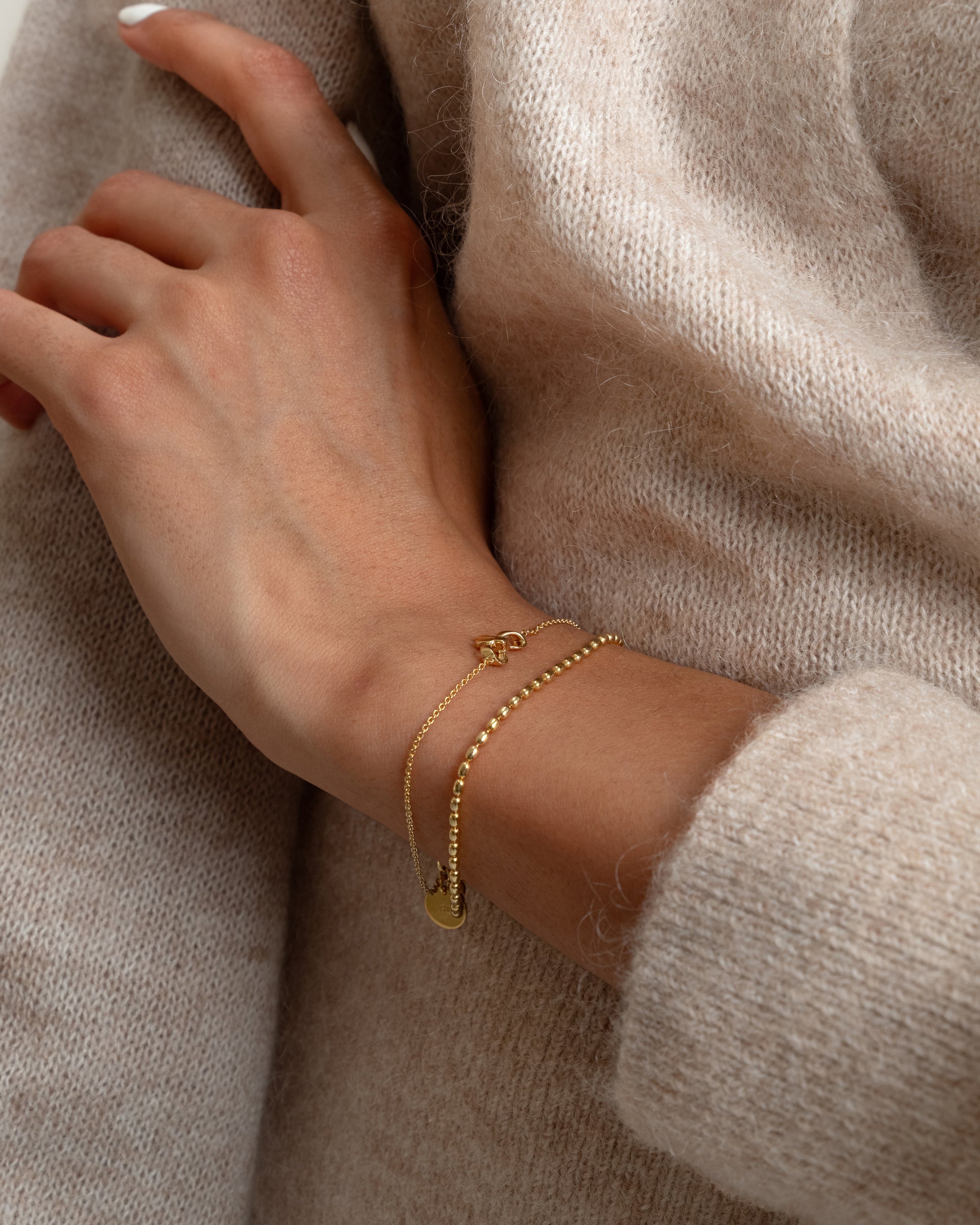A close-up shot of a model wearing the Lunetta Bracelet in gold, featuring its distinctive ball chain with oval beads, stacked with a delicate, fine gold chain bracelet.