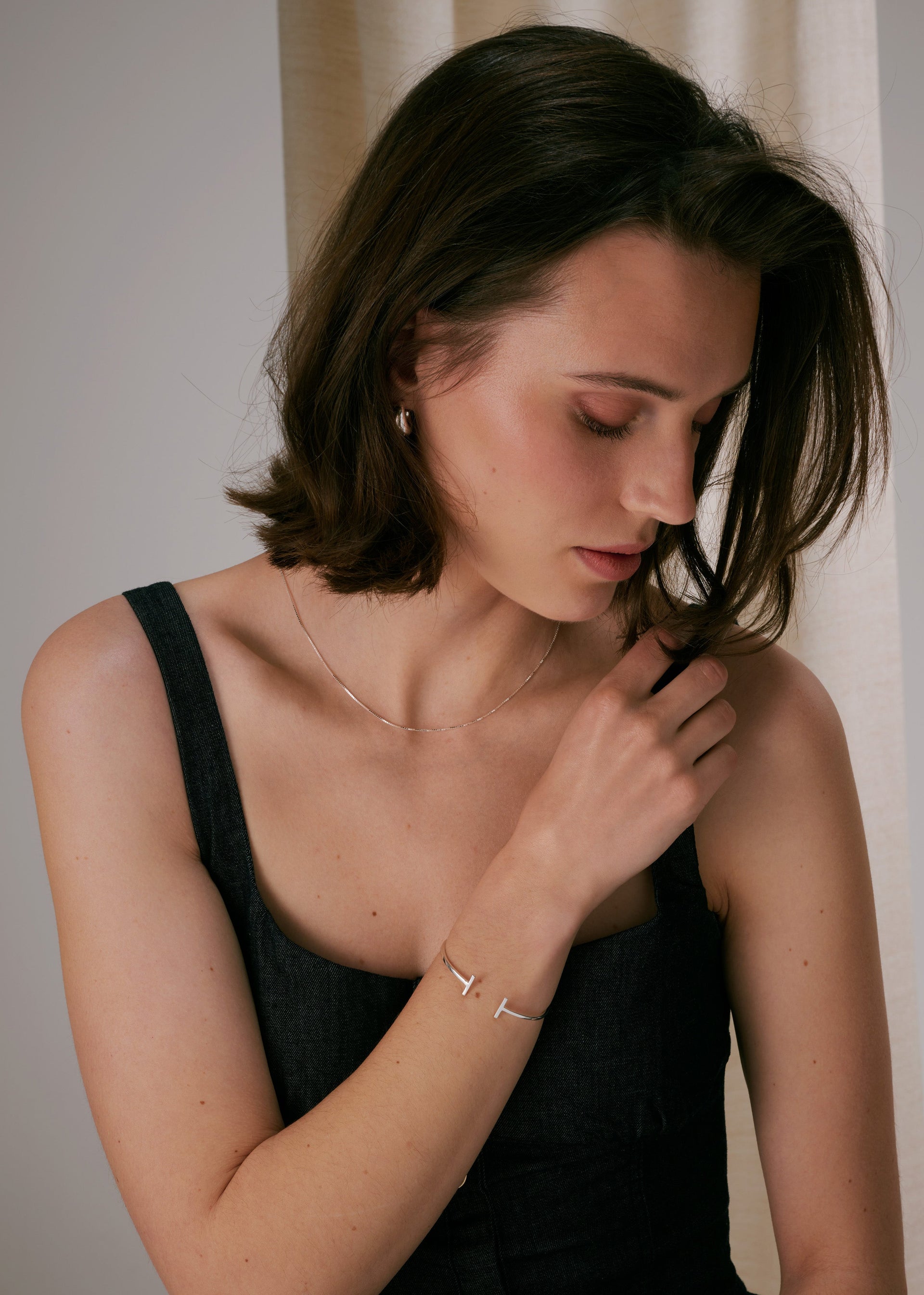 Bangle in silver, paired with a thin silver chain necklace and small silver hoop earrings.
