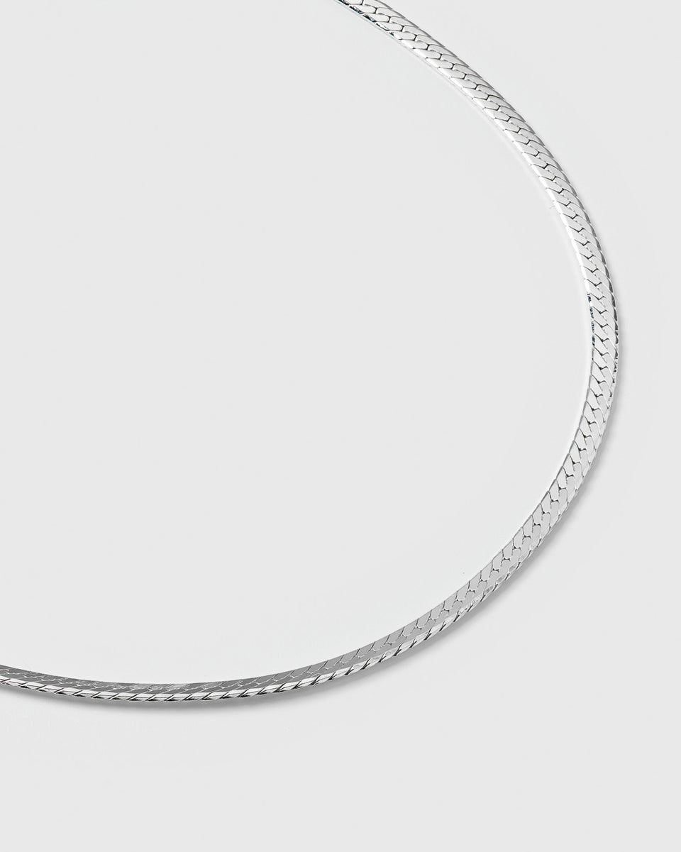 A product shot of the Herringbone Bracelet in silver, laid out in a curve to showcase its smooth, flat, and delicate herringbone chain design.