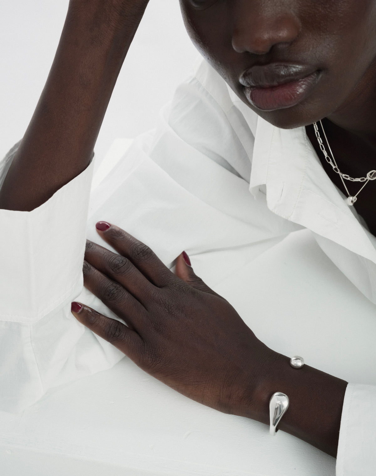A model wearing the Bolded Drops Bangle in silver, a cuff-style bracelet with drop-shaped ends. She is also wearing a layered silver necklace.