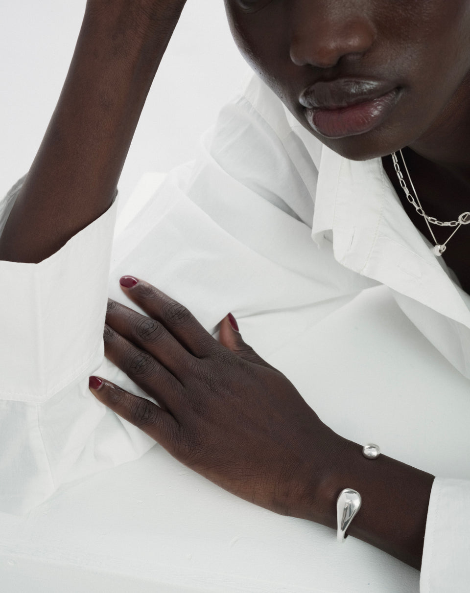 A model wearing the Bolded Drops Bangle in silver, a cuff-style bracelet with drop-shaped ends. She is also wearing a layered silver necklace.