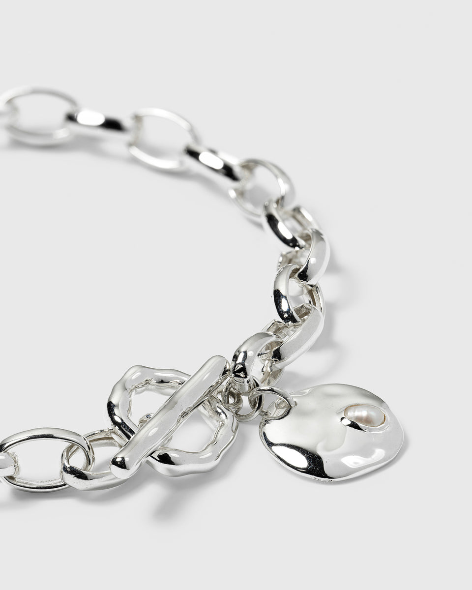 A close-up of the Paxton Heavy Bracelet in recycled sterling silver, showcasing the toggle clasp and the hammered pendant with a small freshwater pearl.