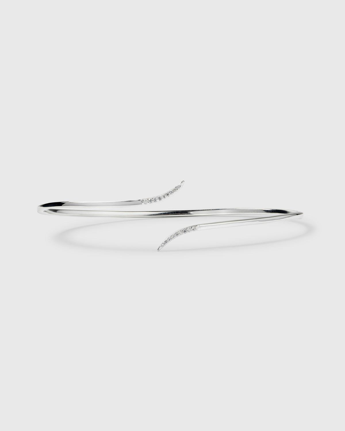A product shot of the Sparkle Wrap Bangle in silver, showcasing its open design where the two curved ends are adorned with sparkling cubic zirconia stones.