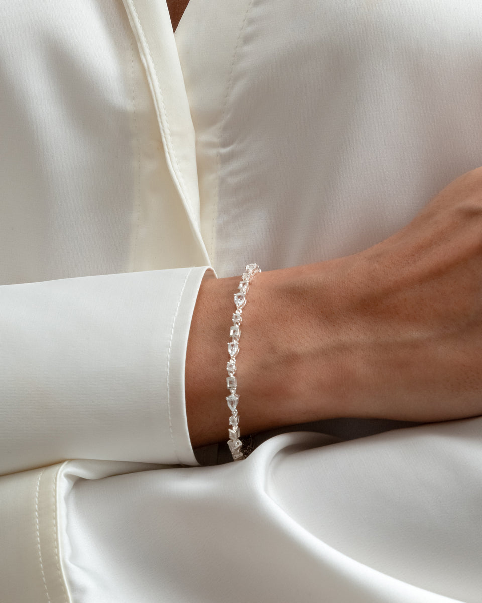 A close-up of a model wearing the Pam Bracelet in silver, highlighting its delicate design of sparkling white topaz stones in various shapes.