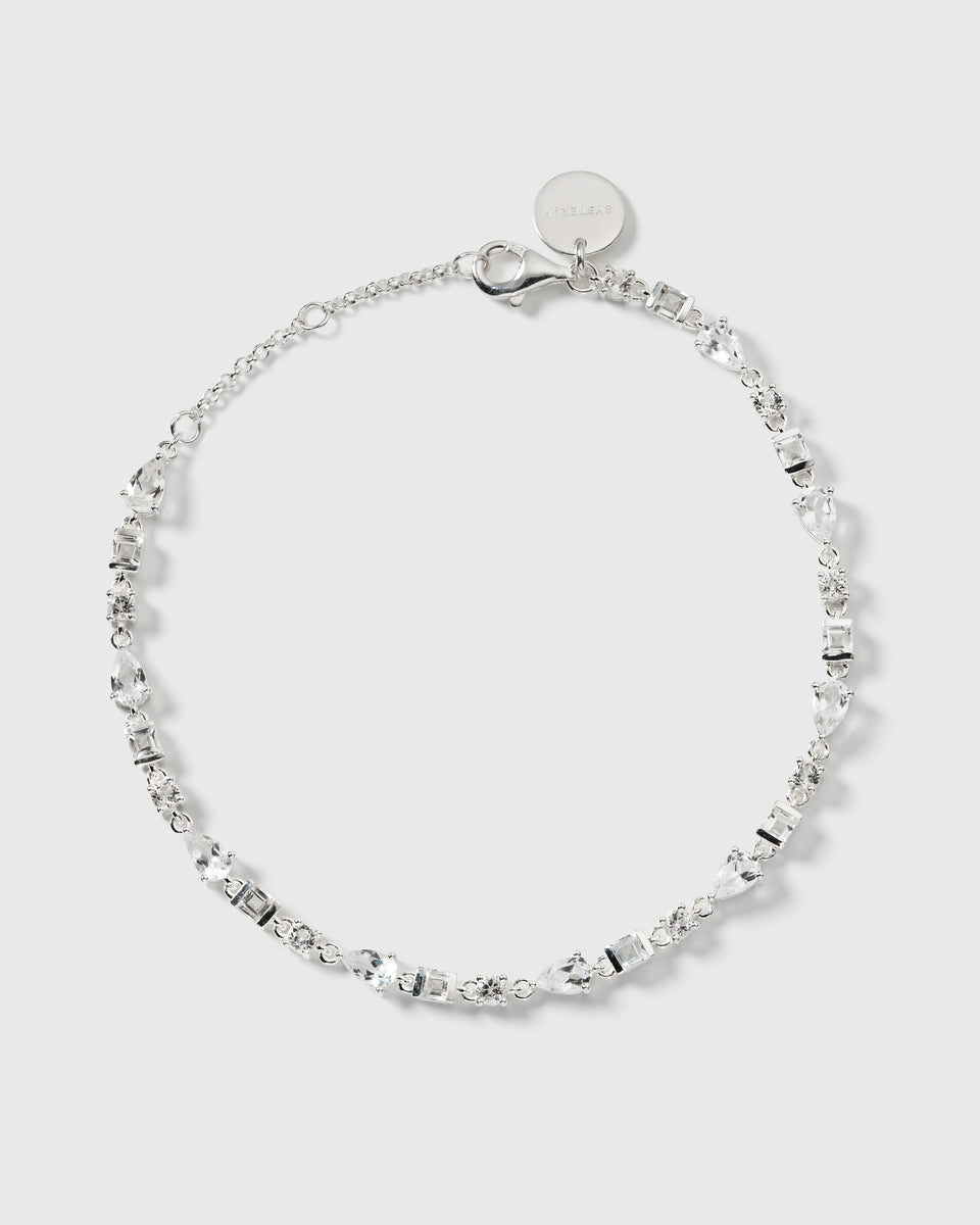 A product shot of the Pam Bracelet in silver, laid out in a circle to display its design of a fine chain adorned with sparkling white topazes of various shapes.