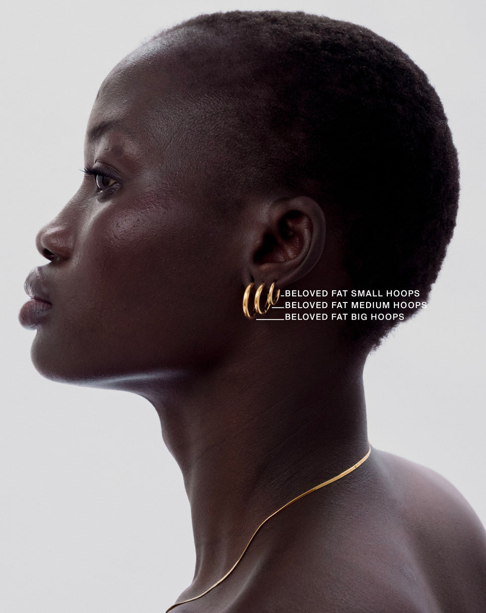 A model in profile wearing three sizes of the Beloved Fat Hoops in gold—small, medium, and big—stacked in her ear, paired with a delicate gold chain necklace.