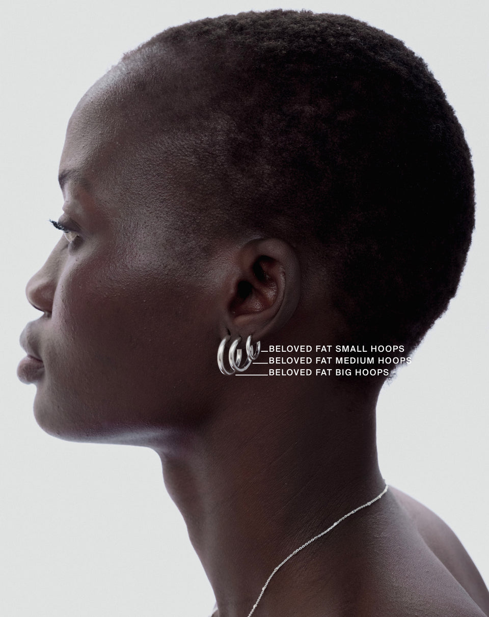 A profile shot of a model wearing three Syster P Beloved Fat Hoops in silver, illustrating the small, medium, and big sizes, paired with a delicate silver chain necklace.
