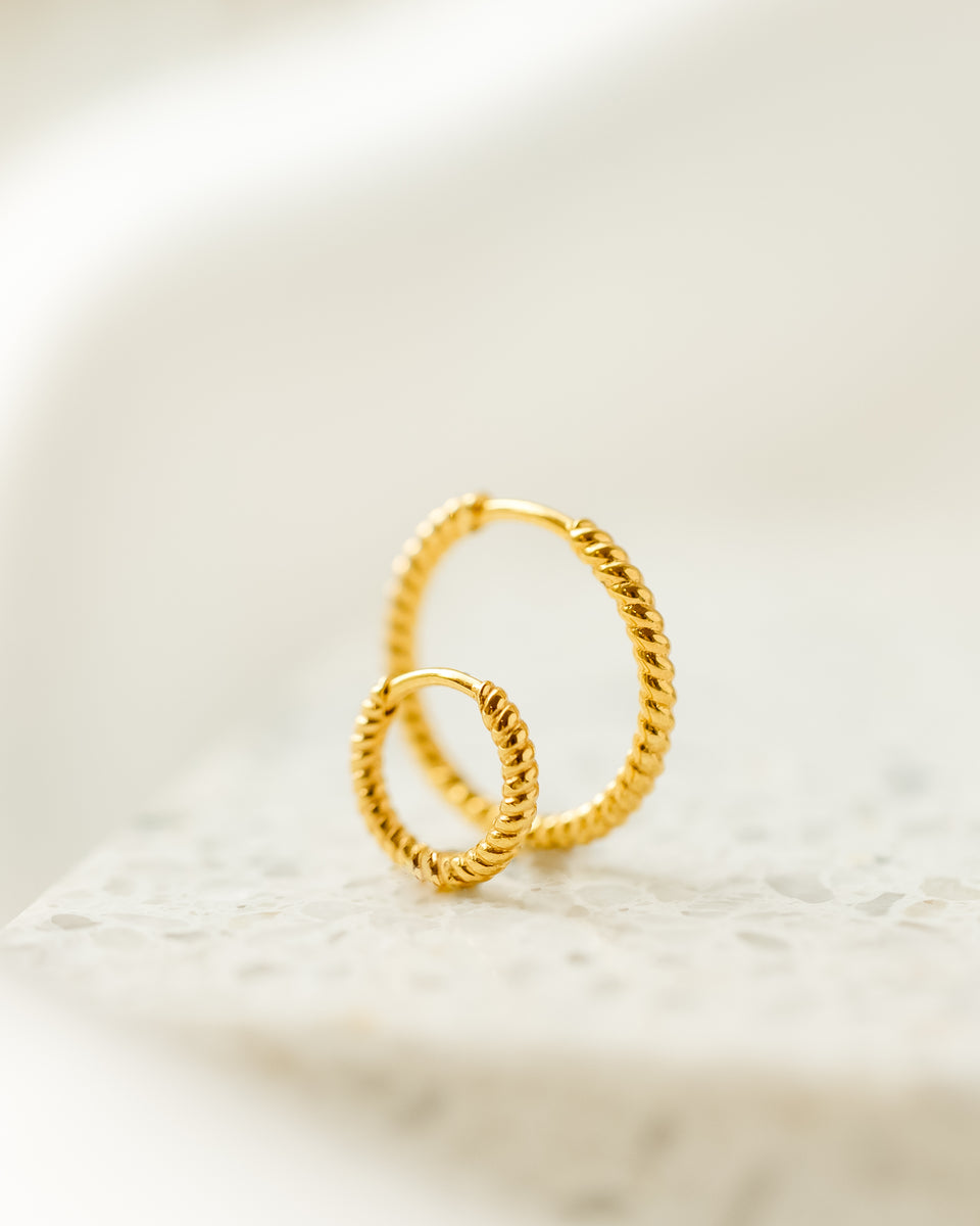 A product shot of the Beloved Twisted Medium Hoops in gold, arranged one in front of the other to showcase their intricate twisted design.
