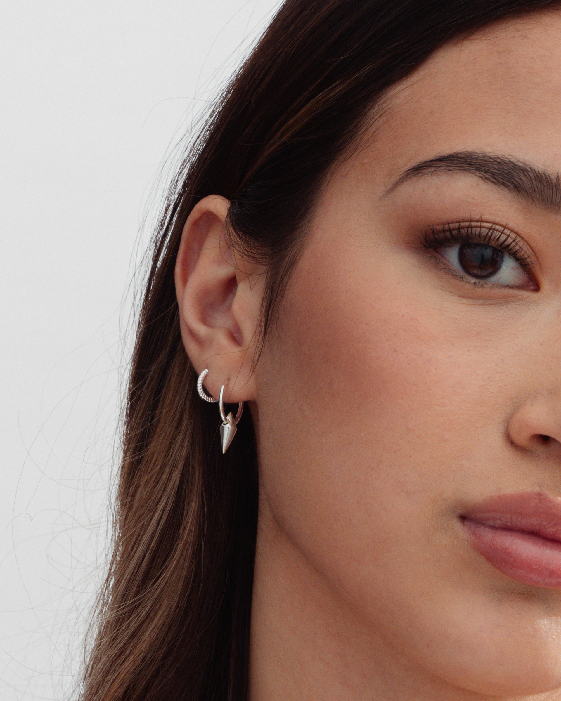A close-up shot of a model wearing two silver earrings: the Beloved Twisted Small Hoops and the Harvey Small Spike Hoops with a dangling spike charm.