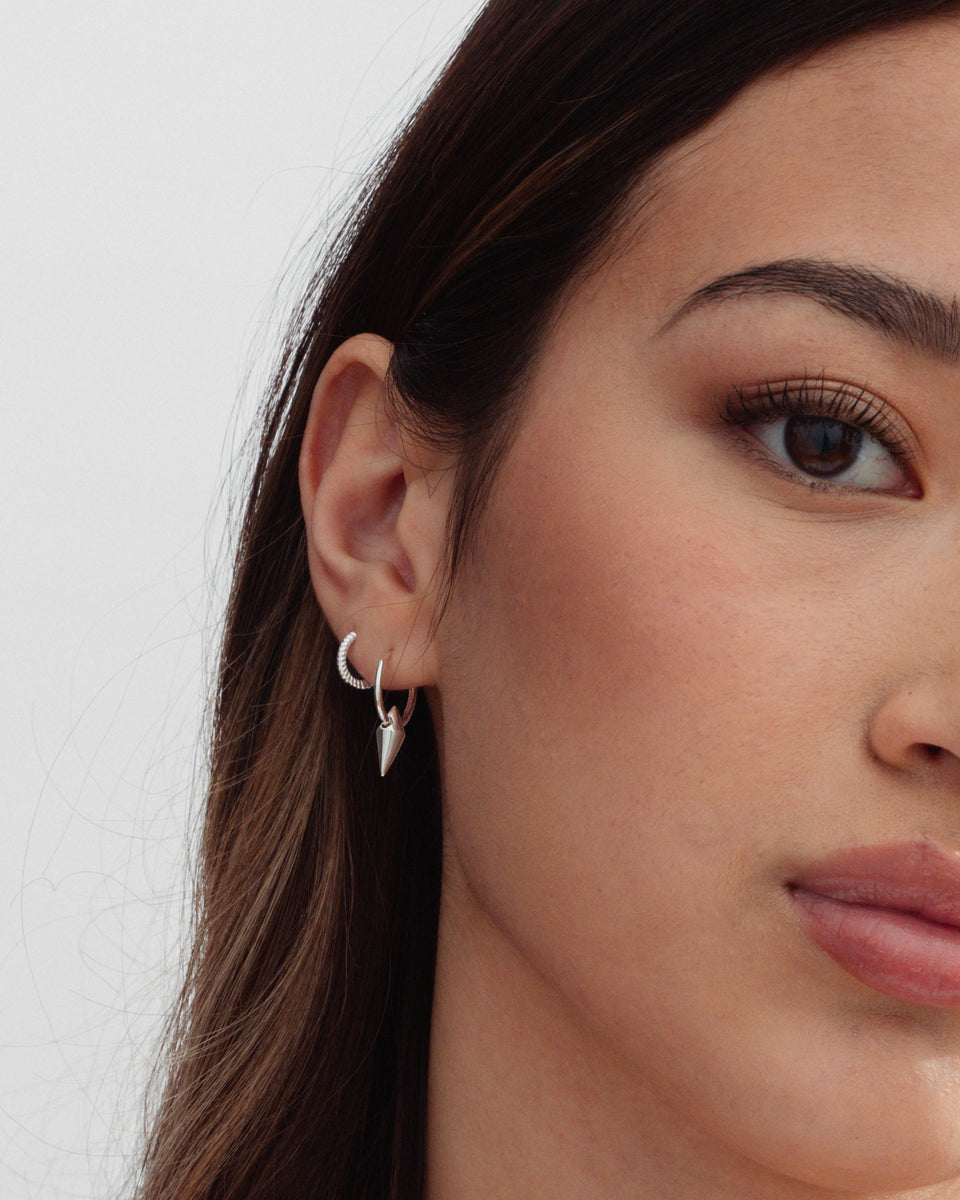 A close-up shot of a model wearing two silver earrings: the Beloved Twisted Small Hoops and the Harvey Small Spike Hoops with a dangling spike charm.