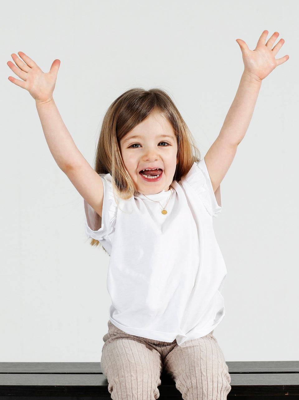 A lifestyle shot of a smiling young girl wearing the Beloved Baby Chain Gold necklace, personalized with a small round letter pendant.