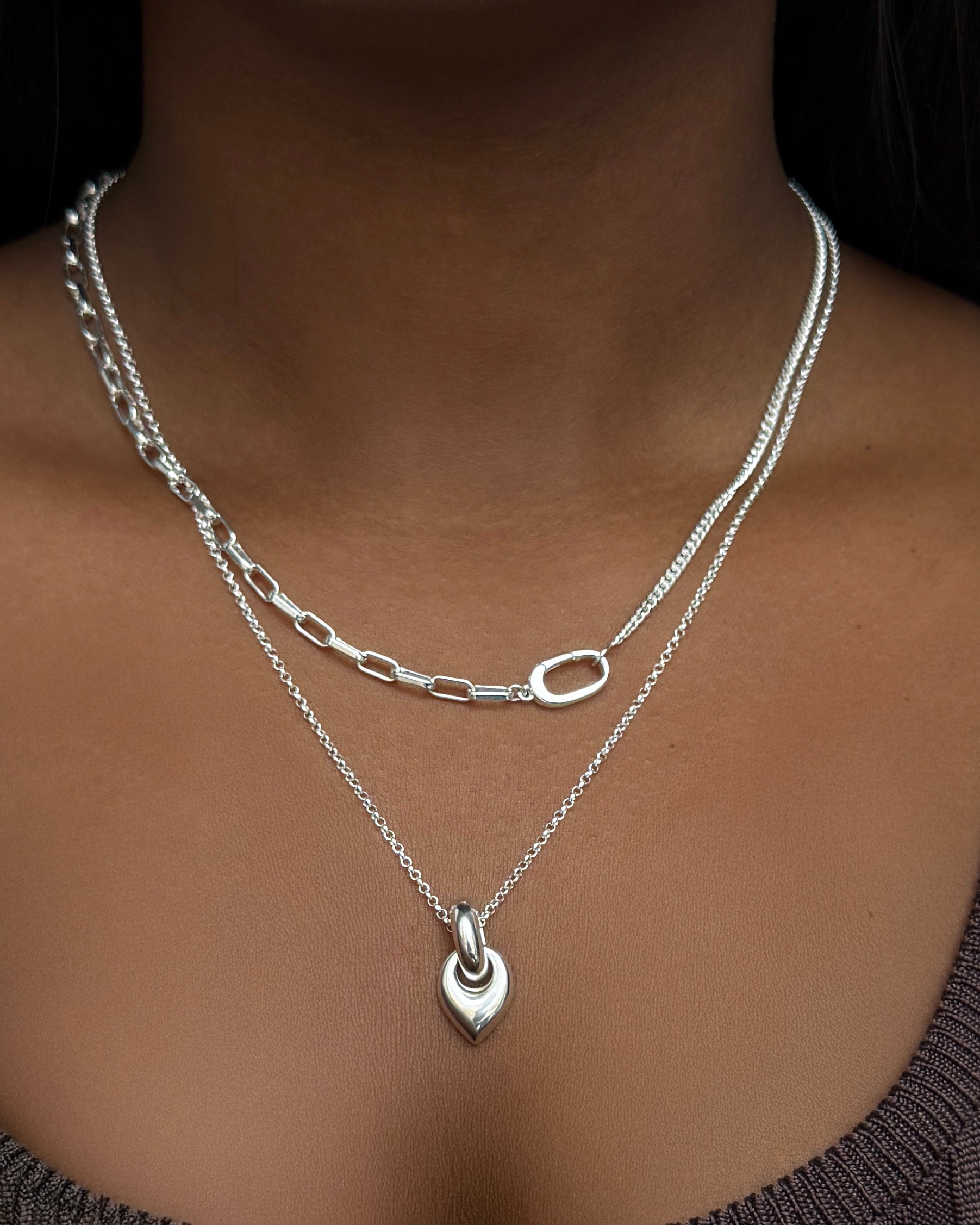 A close-up of a model wearing the silver Harvey Heavy Necklace, featuring a unique mixed-chain design, layered with the silver Melinda Long Necklace with its teardrop pendant.
