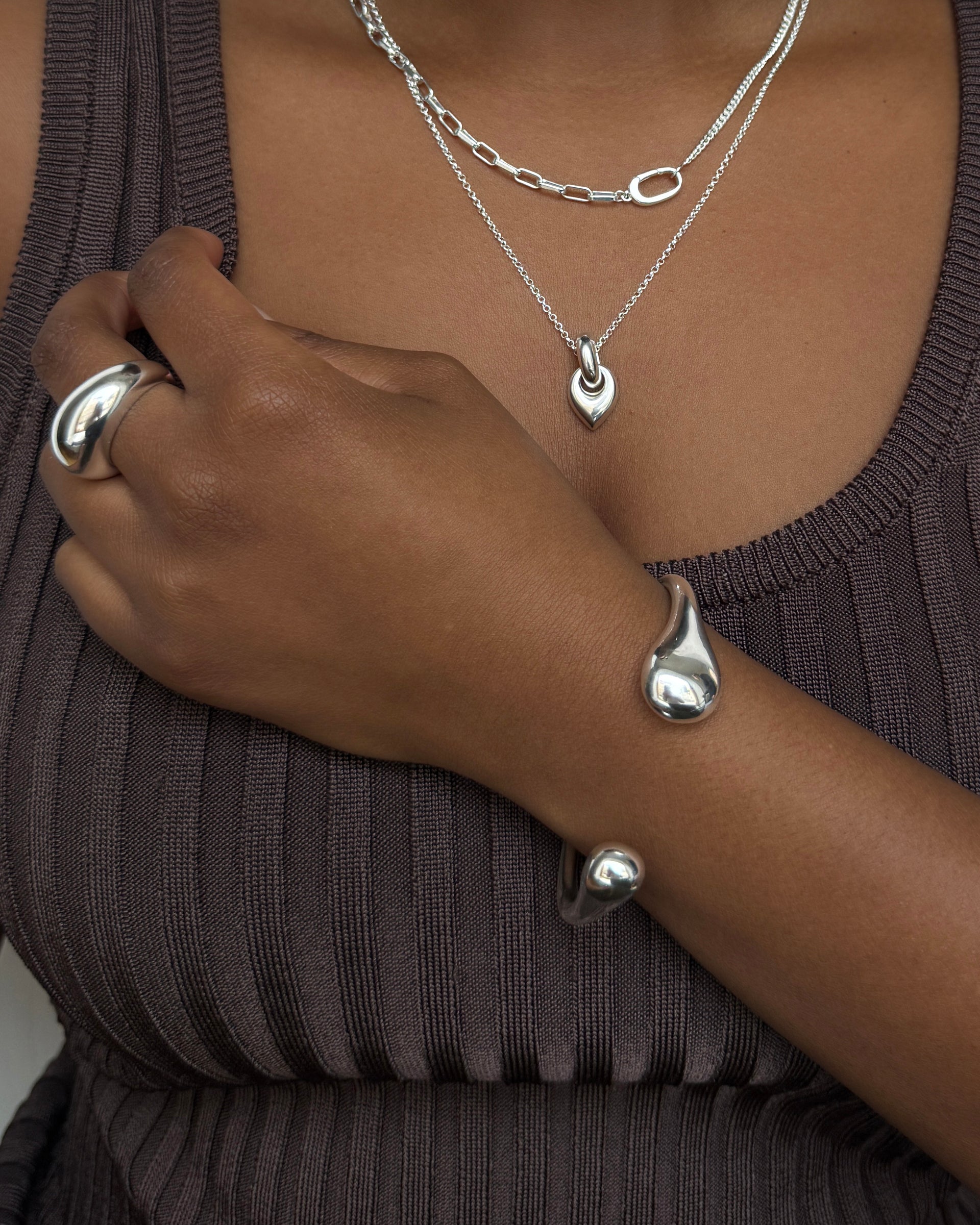 A model wears a curated set of Syster P silver jewelry, including the Bolded Drops Bangle on her wrist, the chunky Bolded Big Ring, and a layered look with the Harvey Heavy chain necklace and the Melinda Long drop pendant necklace.