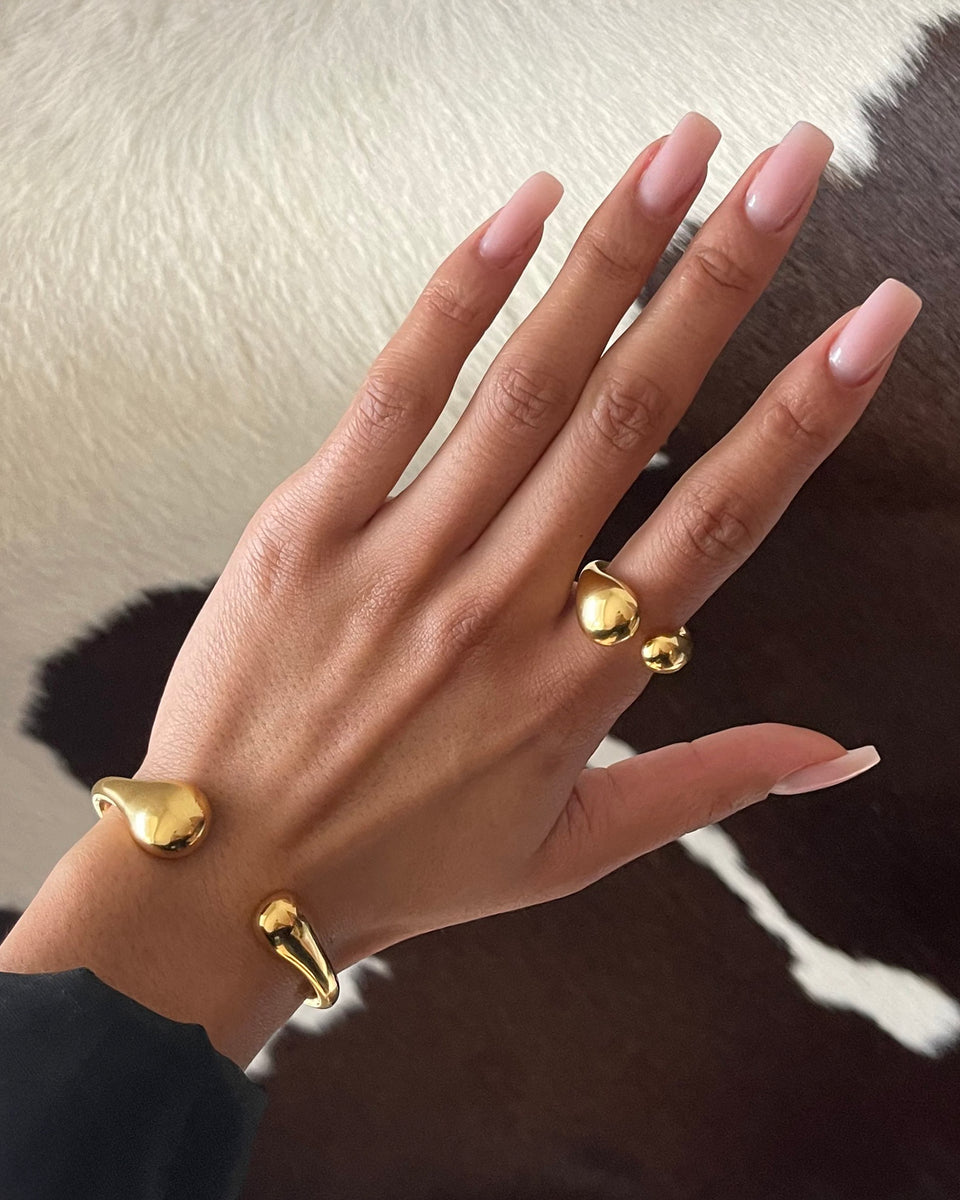 A close-up shot of a model's hand wearing the open-ended Bolded Drops Ring in gold, paired with the matching Bolded Drops Bangle on her wrist.
