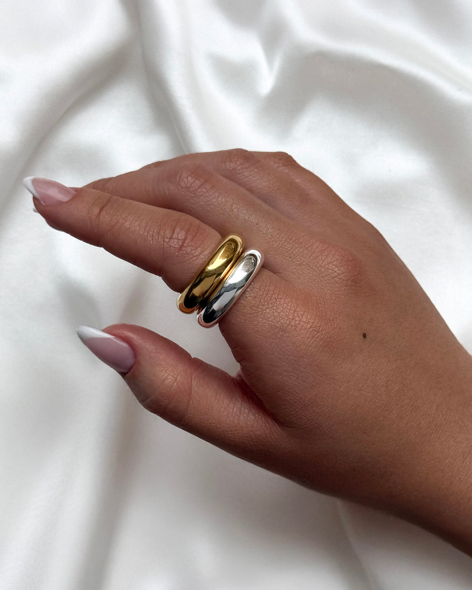 A close-up shot of a model wearing the Bolded Ring in gold stacked with the Bolded Ring in silver on her ring finger.