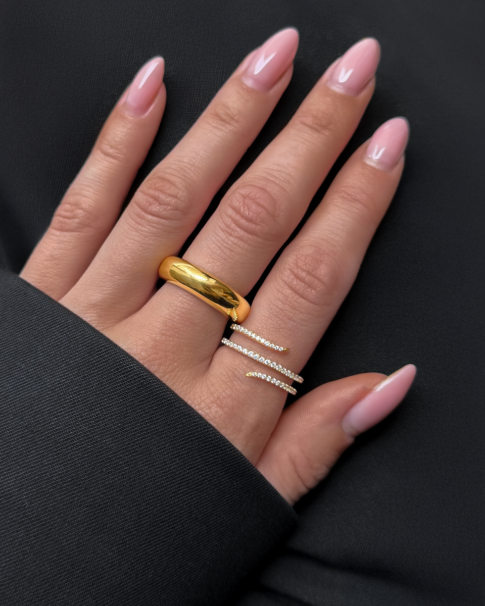 A close-up of a model's hand wearing the Bolded Ring in gold, styled with the Wrapt Sparkle Ring, a gold wrap-around ring paved with sparkling crystals.