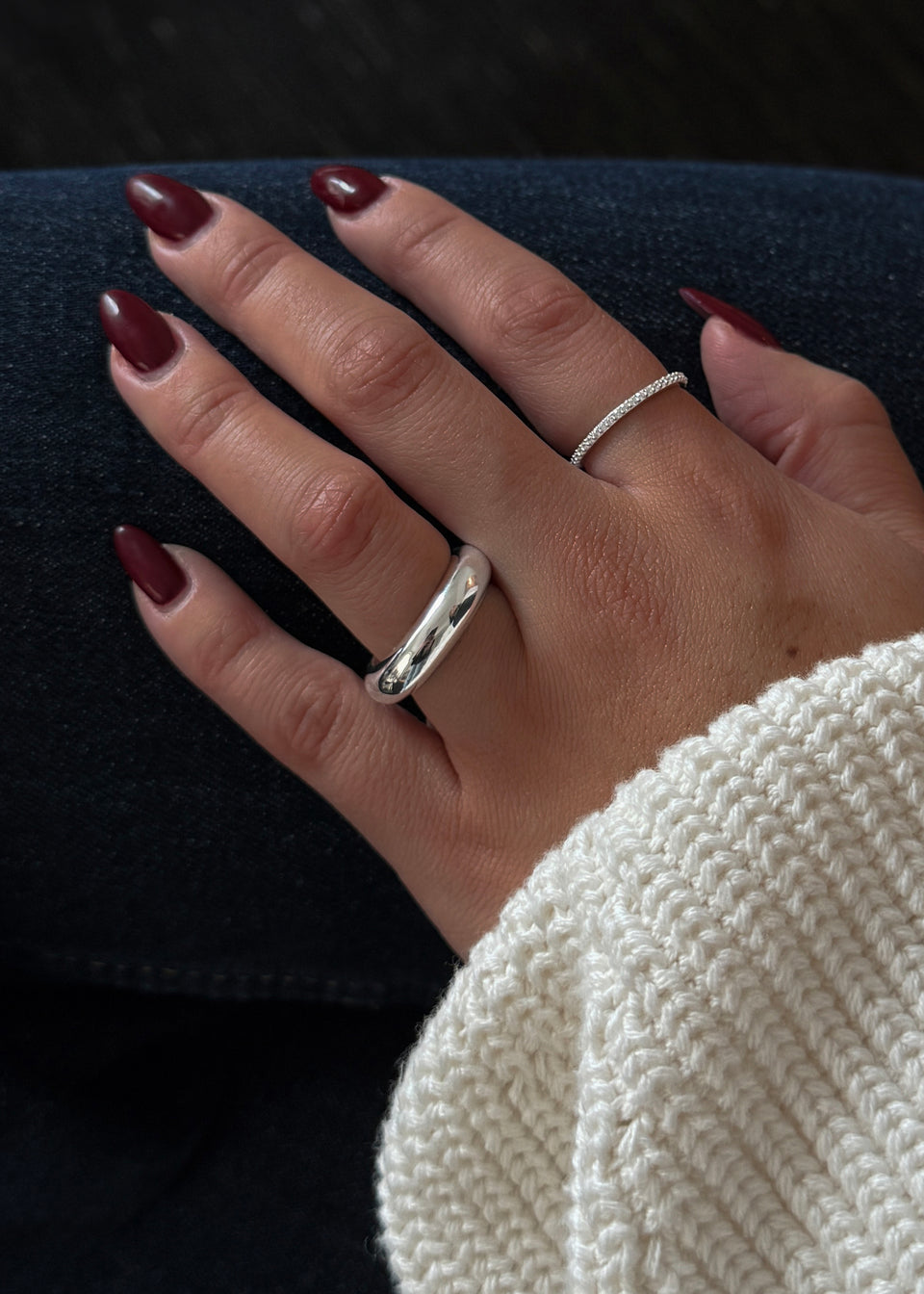 A close-up of a model's hand wearing the chunky Bolded Ring in silver on her middle finger, styled with the delicate Tiny Sparkle Ring in silver on her ring finger.