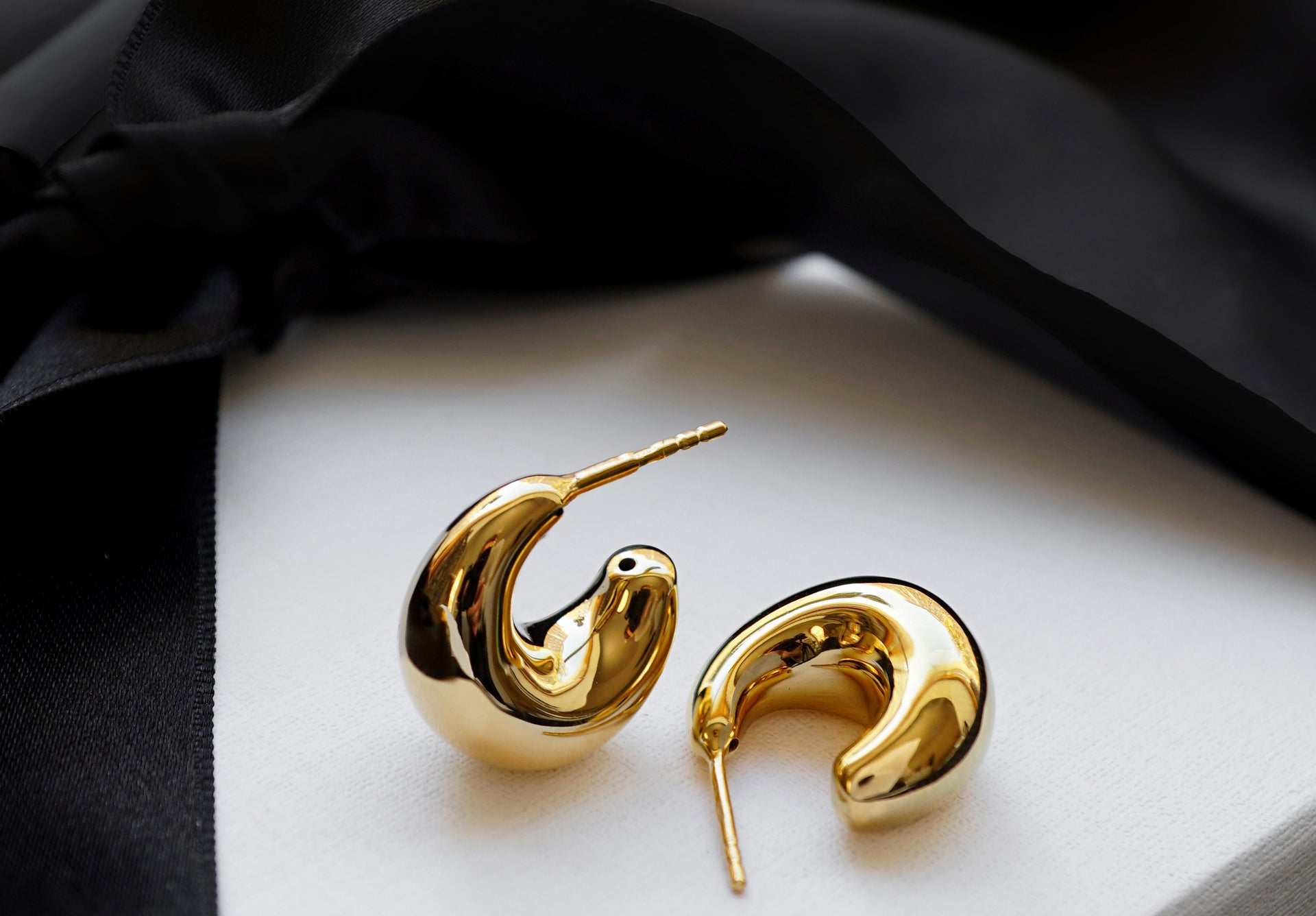 Chunky earrings in gold on top of a giftbox