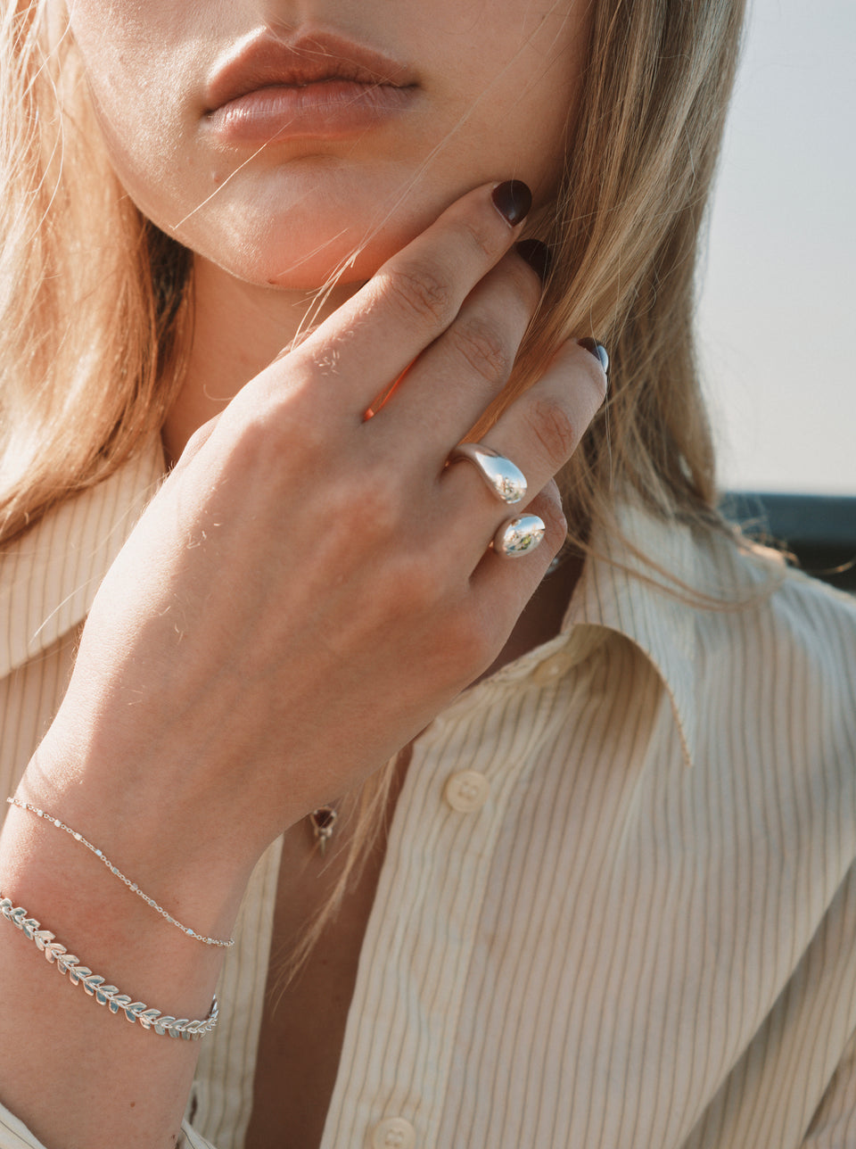 A close-up of a model wearing the Bolded Drops Ring, Olivia Bracelet, and Sheer Station Bracelet, all in silver.