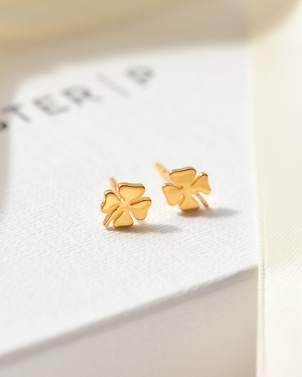A product shot of the Bring Me Luck Studs in gold, featuring a four-leaf clover design, resting on a white Syster P jewelry box.