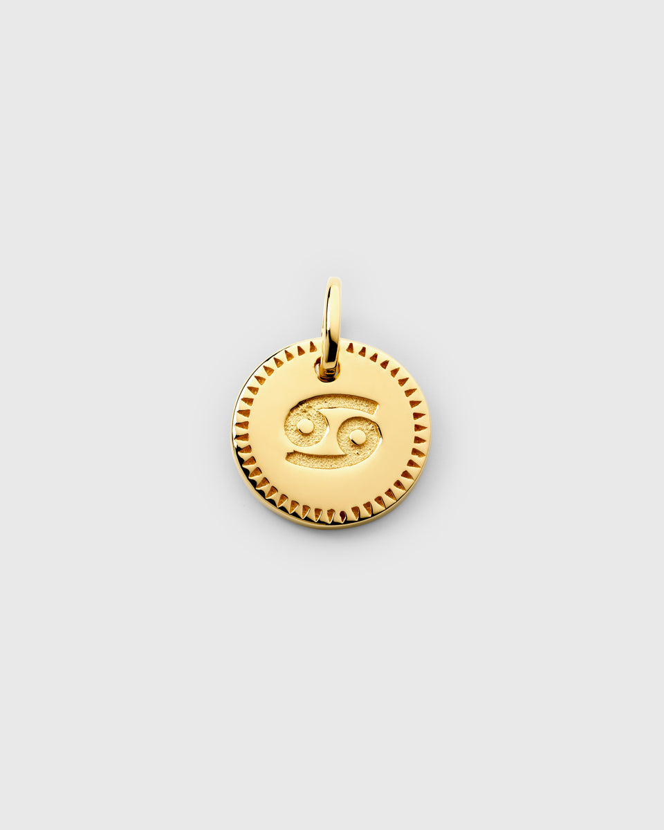 A product shot of the gold Beloved Zodie Pendant, showcasing the Cancer variant. The round charm has the Cancer zodiac symbol engraved in the center and is framed by a decorative border.