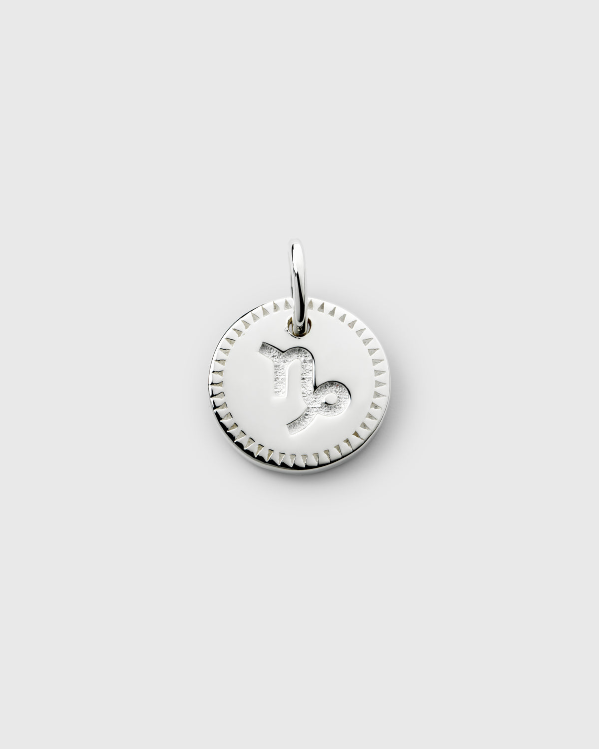 A product shot of the Beloved Zodie Pendant in silver, showcasing the Capricorn charm with its engraved symbol and decorative triangular-patterned border.
