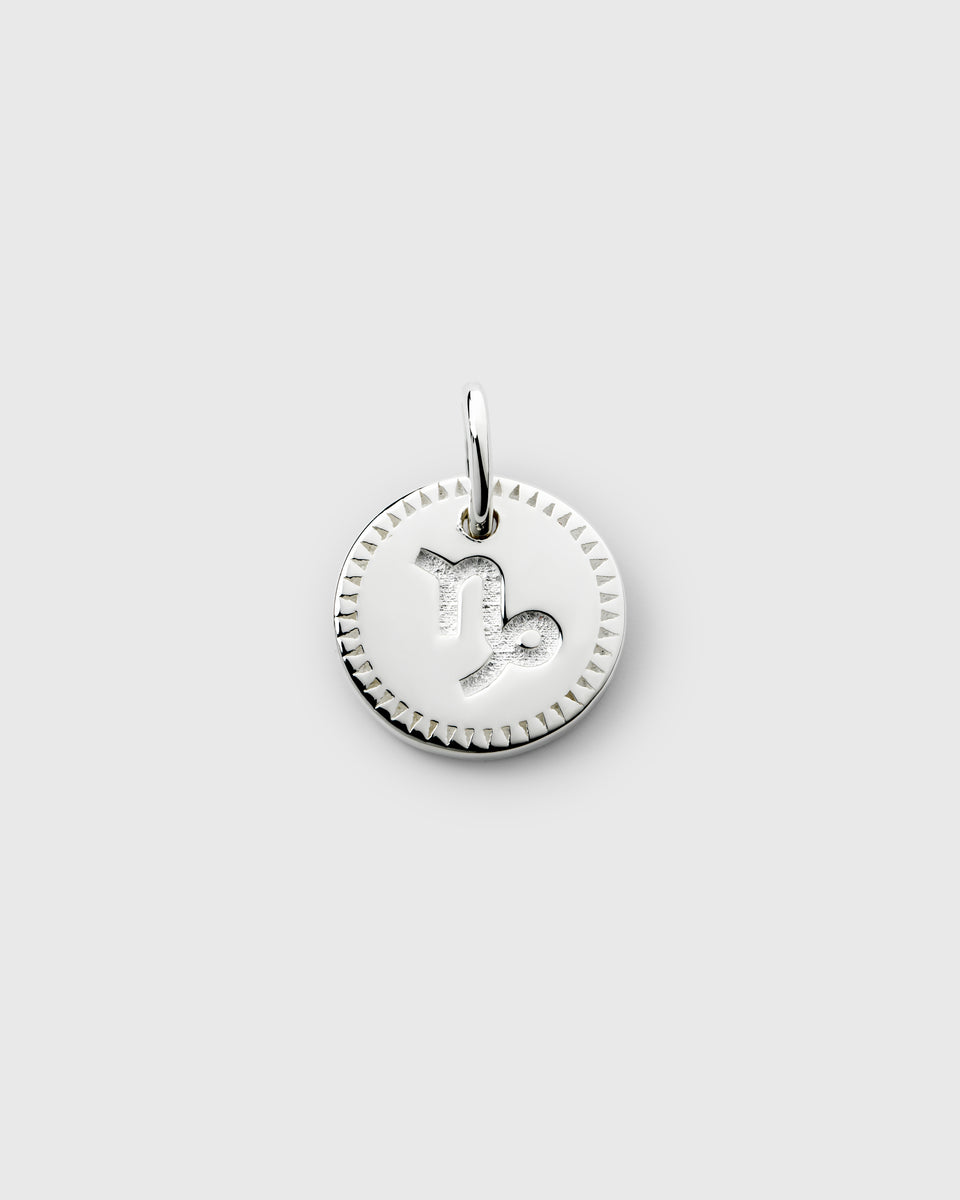 A product shot of the Beloved Zodie Pendant in silver, showcasing the Capricorn charm with its engraved symbol and decorative triangular-patterned border.