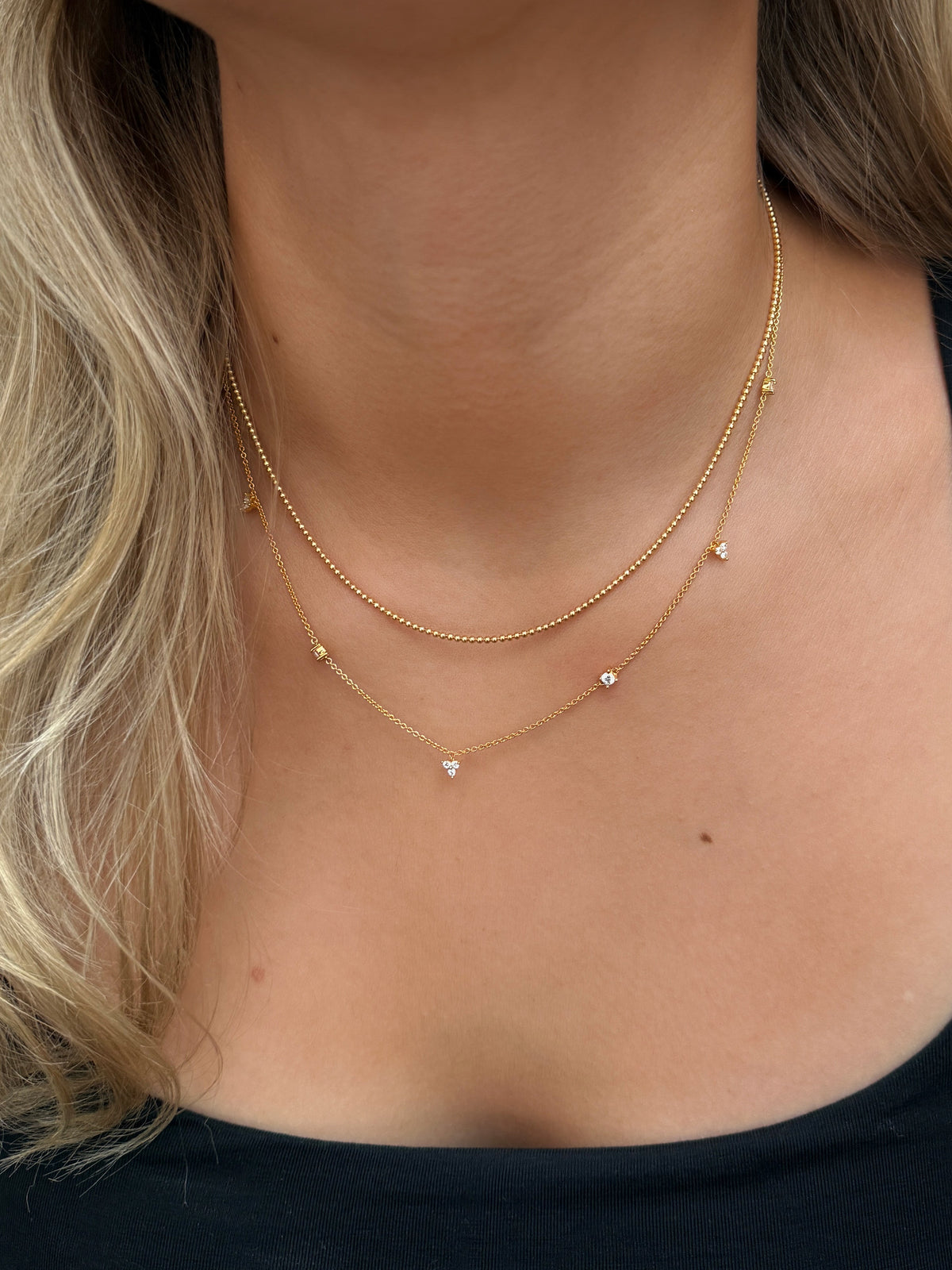 Layered gold necklaces with delicate beaded chain and fine chain with cubic zirconia stones.