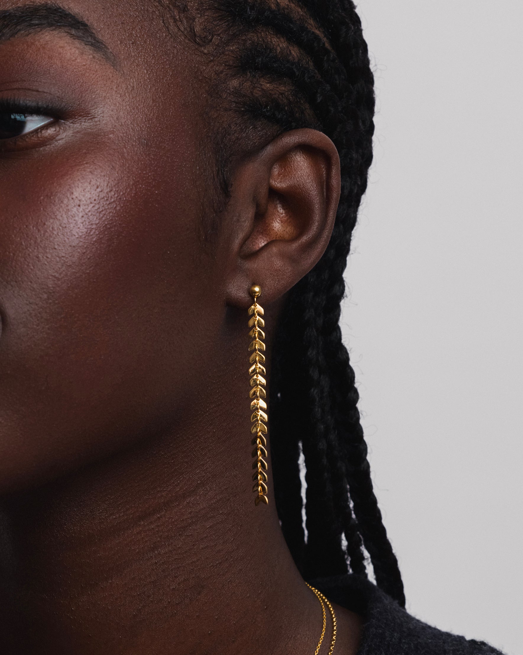 Close-up of a model wearing the Layers Olivia Earrings in gold, which dangle with a cascade of small leaf-like charms. 