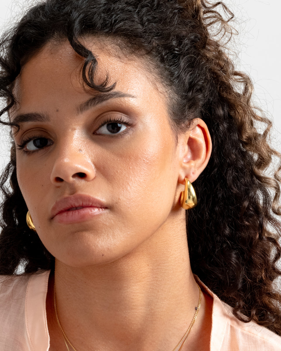 A close-up shot of a model wearing a pair of chunky, crescent-shaped earrings with a polished finish.