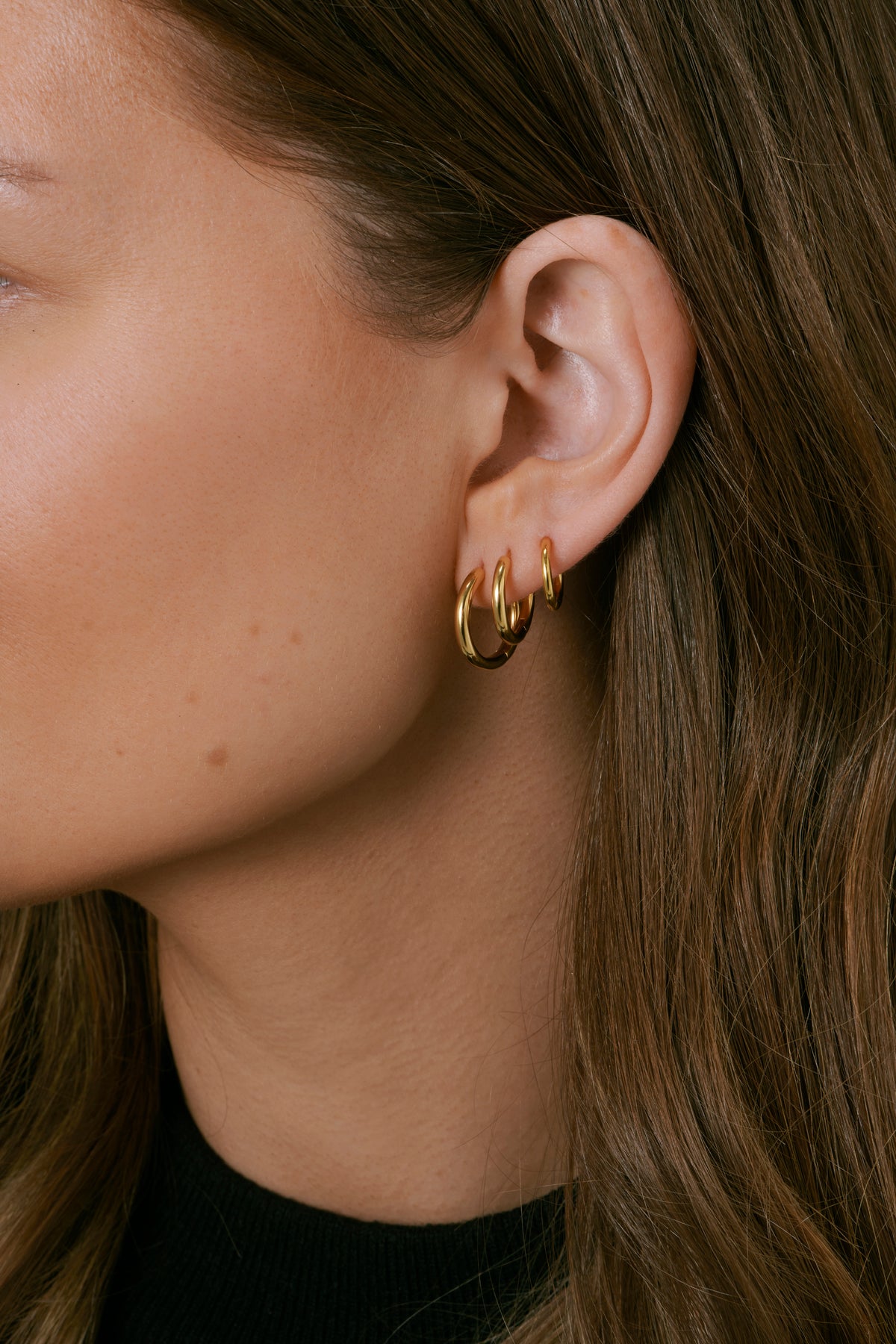 A side profile shot of a model wearing the Beloved Fat Small, Medium, and Big Hoops in gold stacked in her ear.