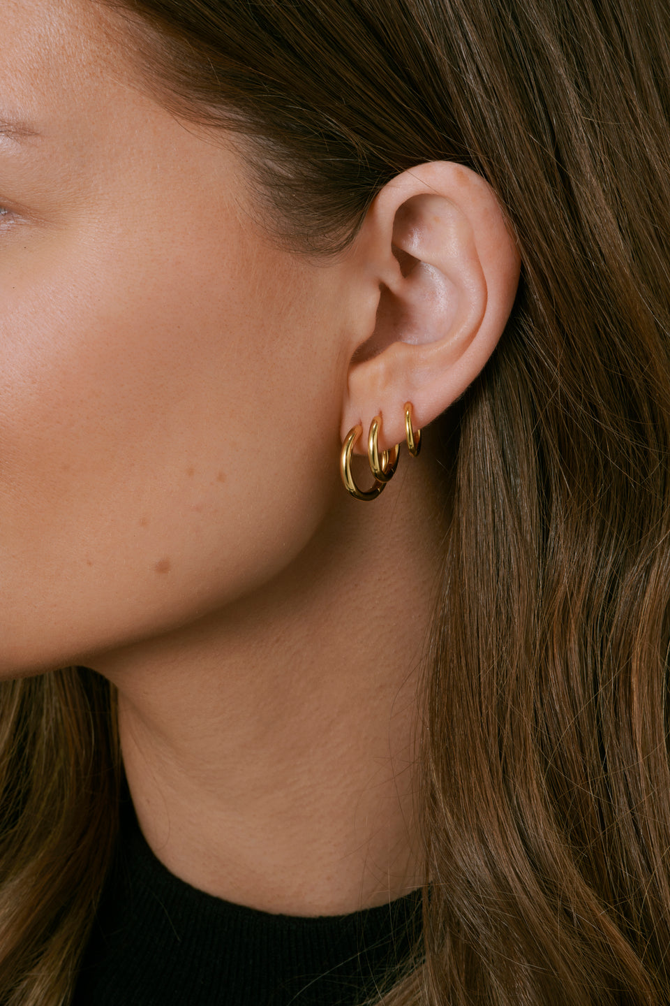A side profile shot of a model wearing the Beloved Fat Small, Medium, and Big Hoops in gold stacked in her ear.