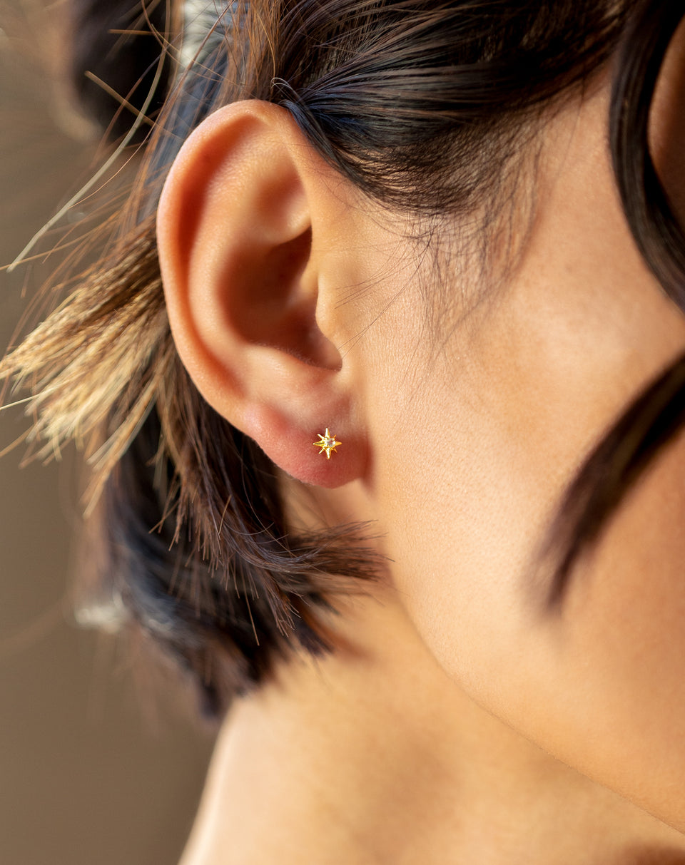 A close-up of a model wearing the North Star Stud Earring in gold, featuring a star design with a central faceted crystal.
