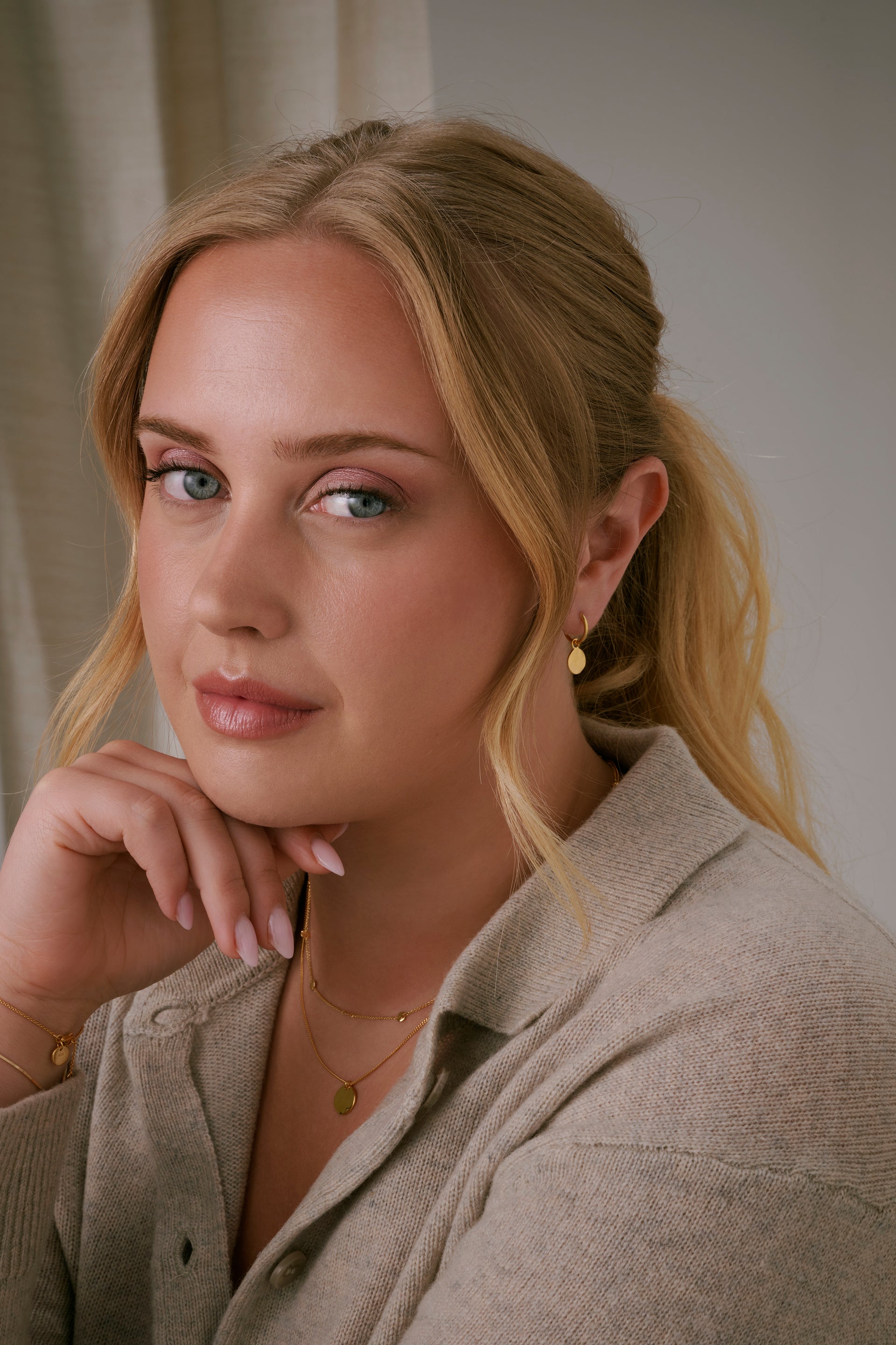 A shot of a model wearing the Minimalistica Hammered Earrings in gold, featuring a small hoop with a dangling, round pendant with a hammered surface.