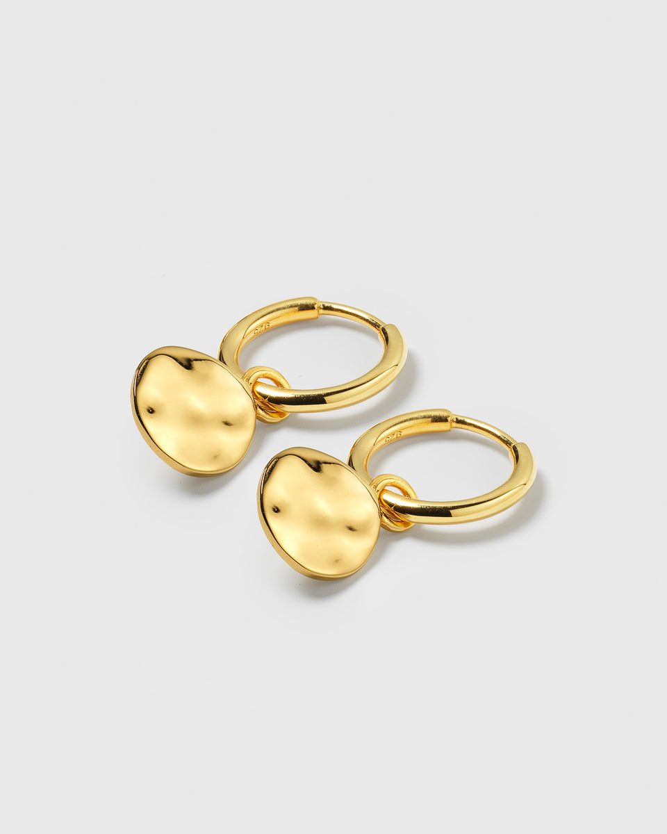 A product shot of the Minimalistica Hammered Earrings in gold, displaying the pair of small hoops with their dangling, round pendants that have a hammered surface.
